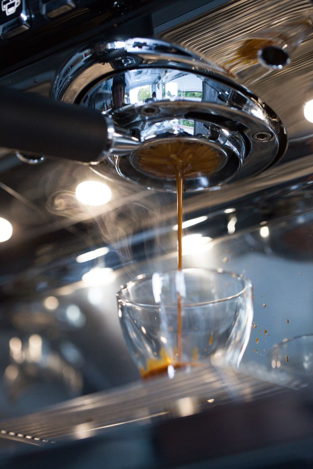 Coffee streaming from an espresso machine into a clear glass cup with steam and lighting effects.