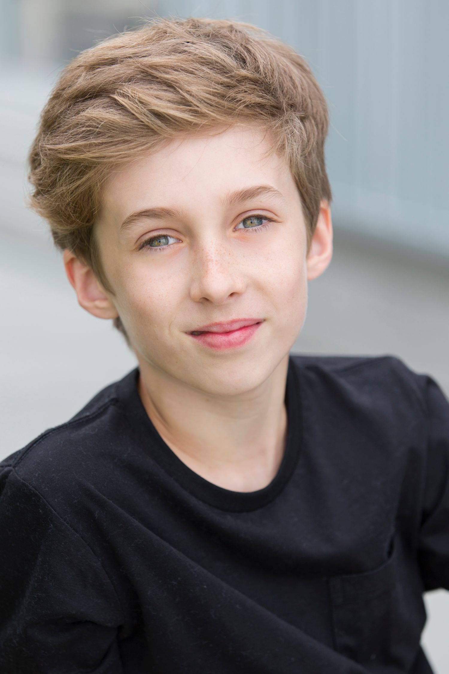 Young person in black sweater smiles playfully at camera in portrait series.