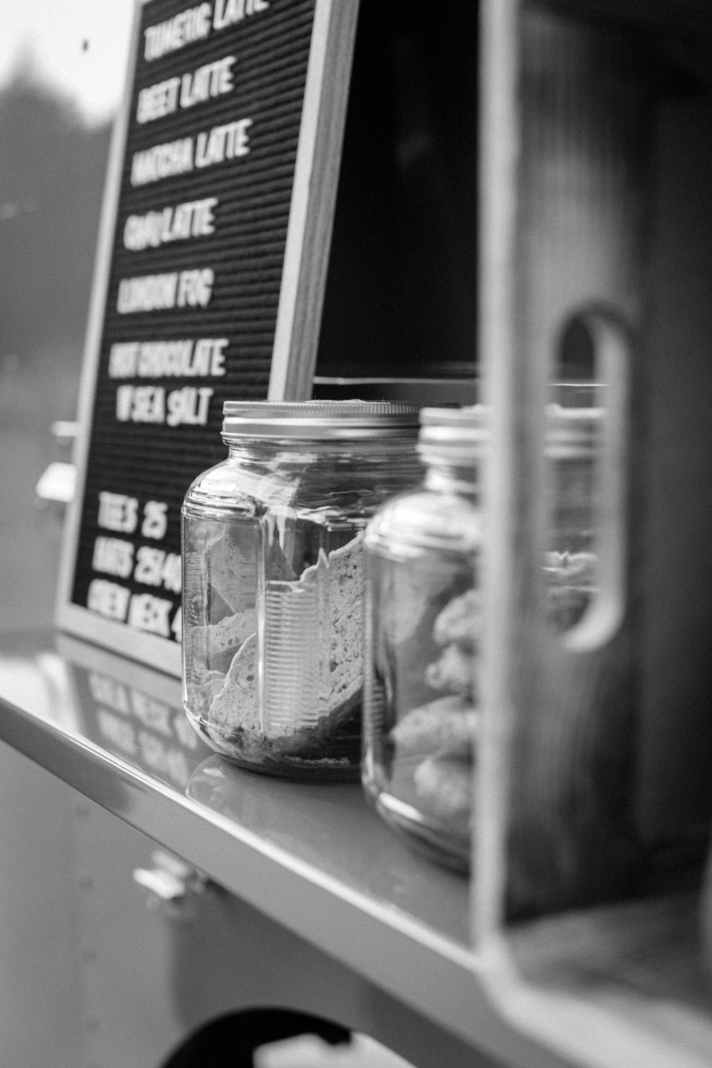 Black and white image of mason jars on shelf next to menu board at coffee shop.