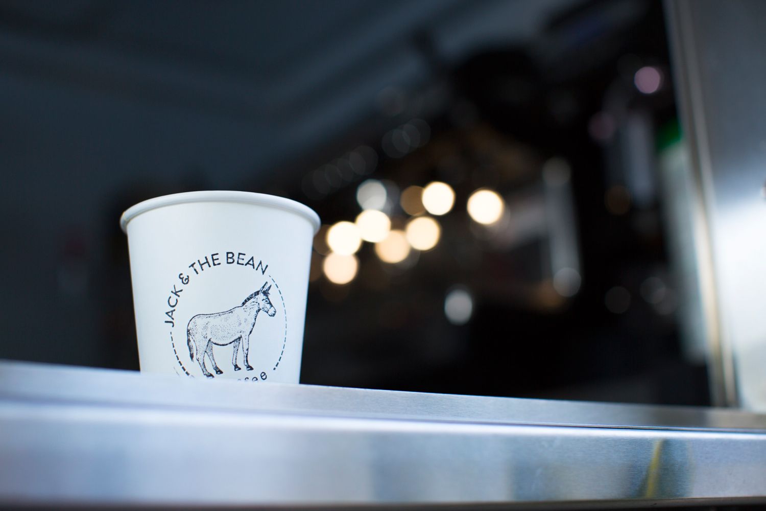 White coffee cup with donkey logo on shelf with bokeh lights in background.