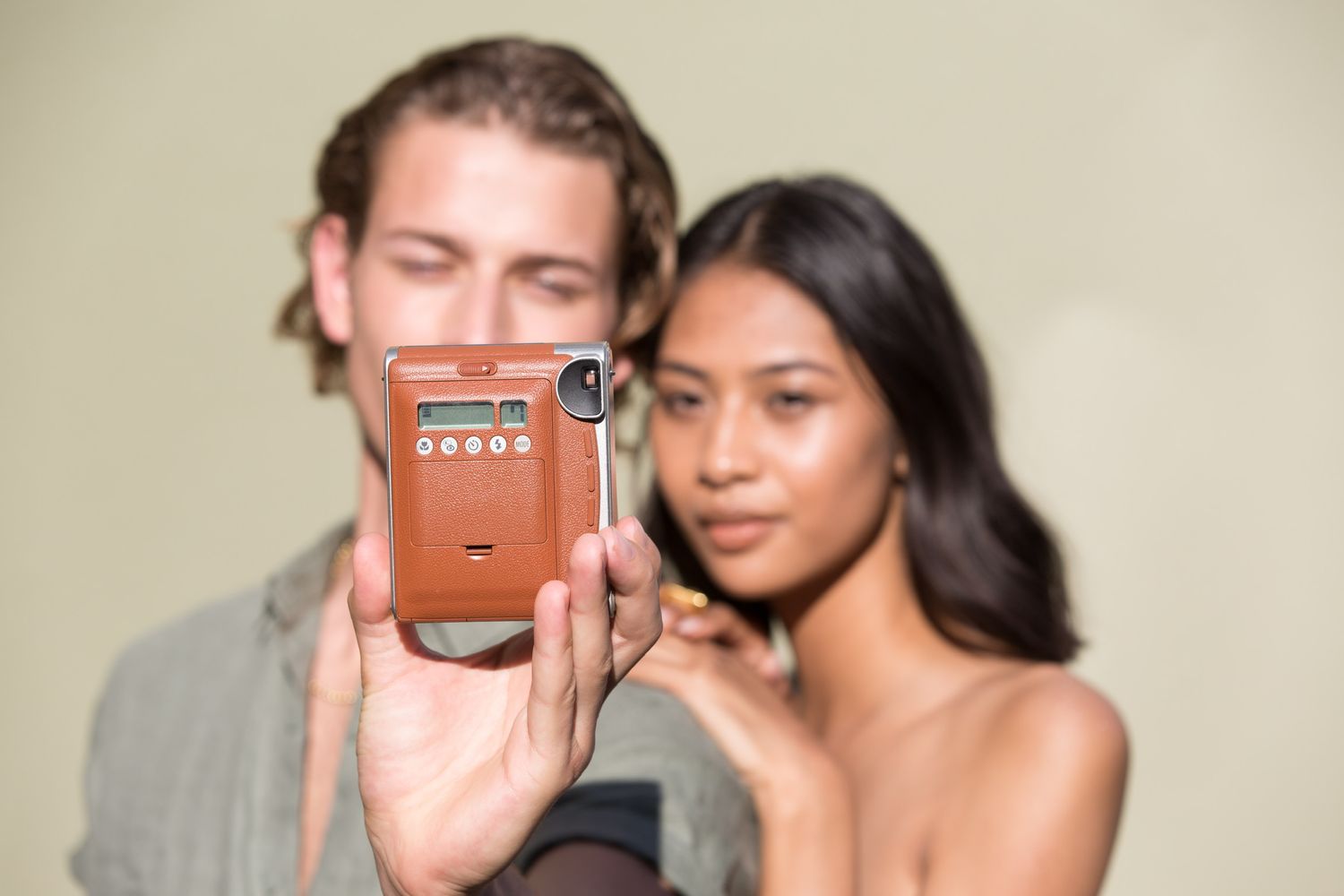 People posing with a retro orange camera against beige background.