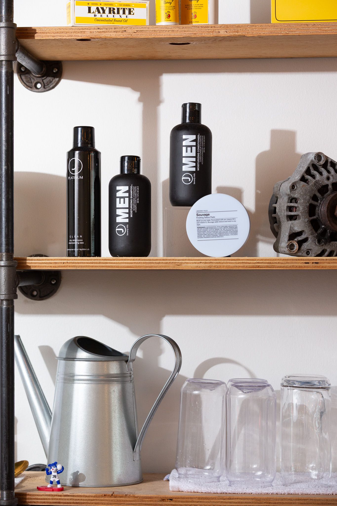Wooden shelf displaying men's grooming products and glass containers with industrial pipe fixtures.