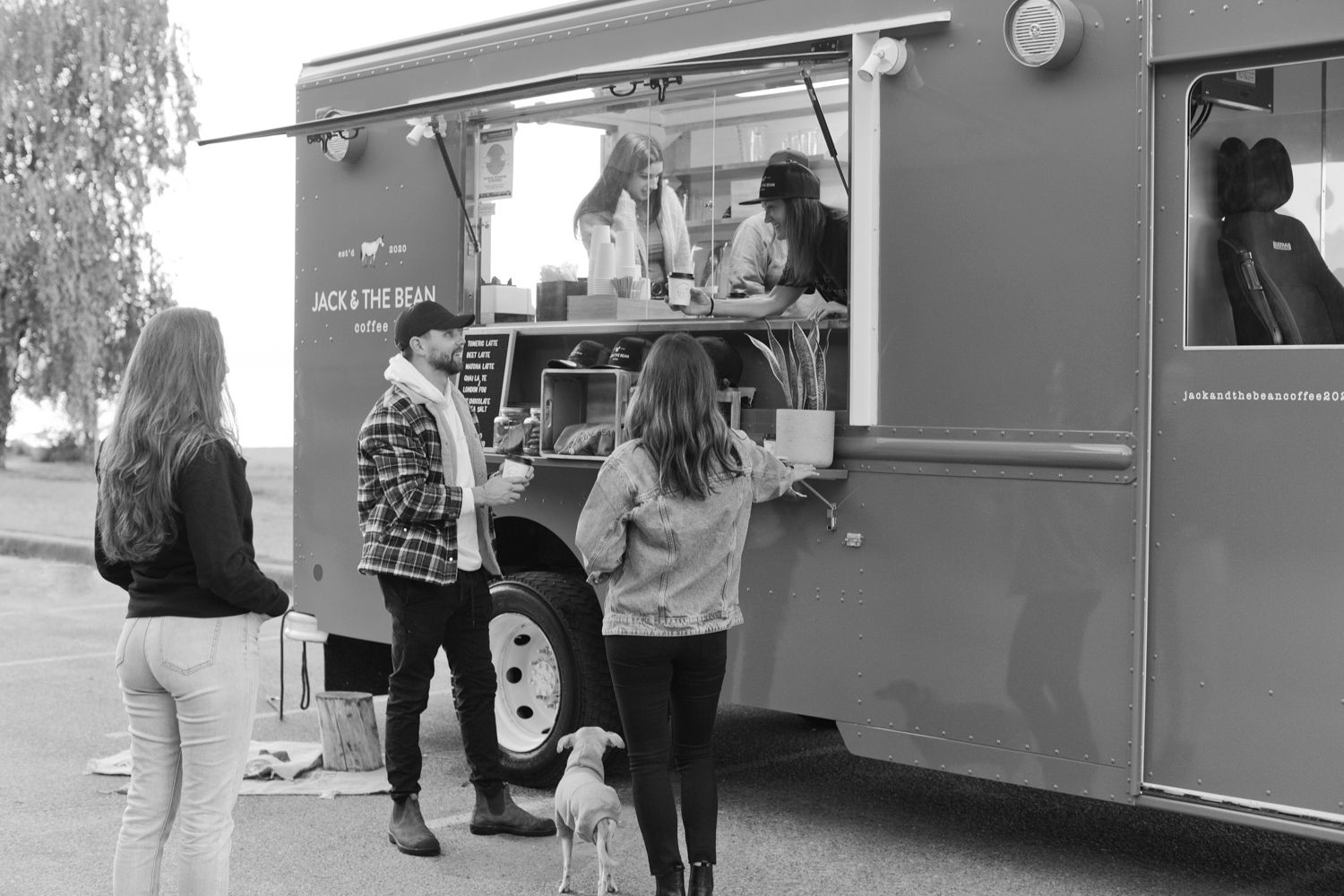 Customers line up at a mobile coffee truck to place their orders on a sunny day.