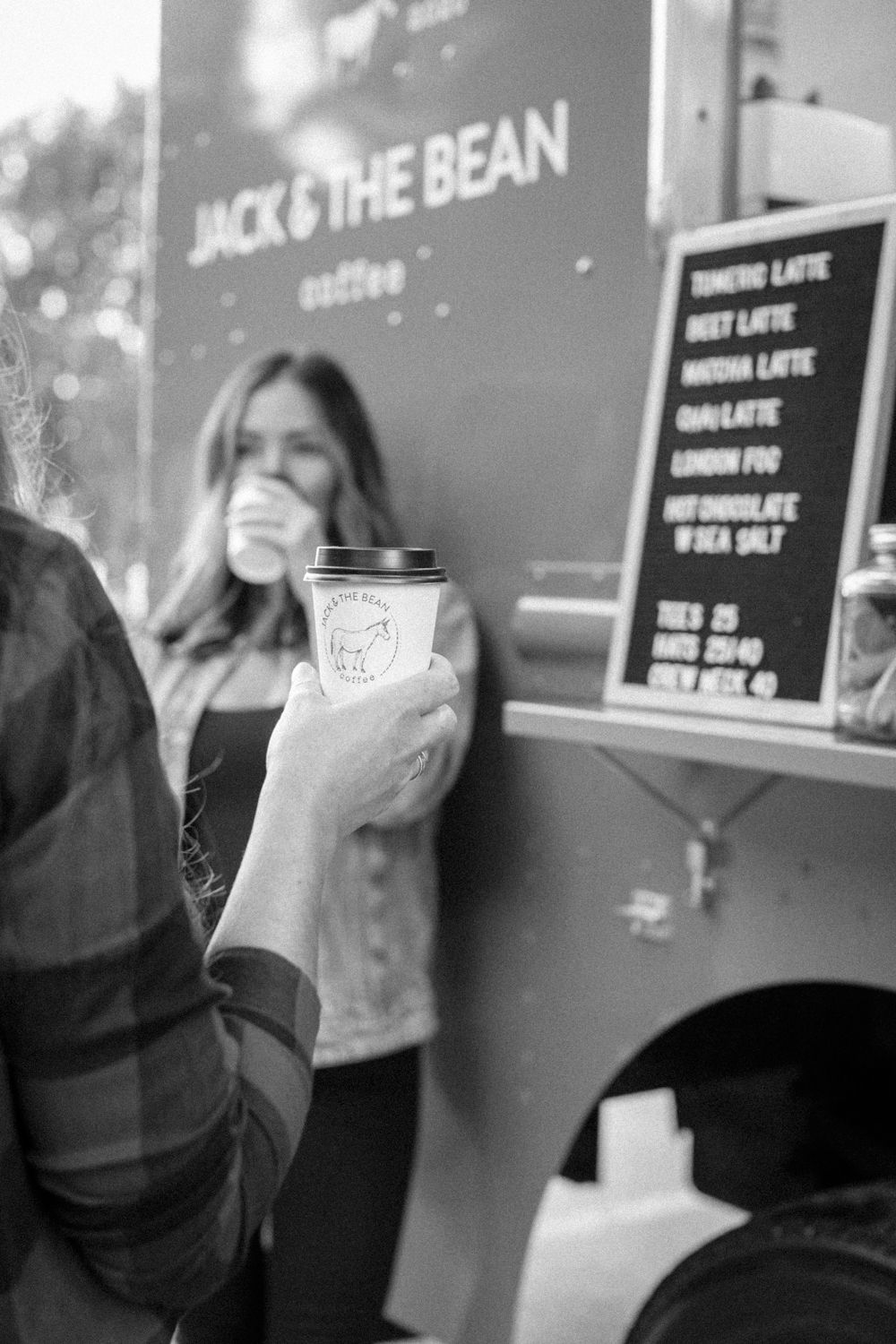 Hand holding a coffee cup in front of Jack & The Bean coffee truck with menu board visible.