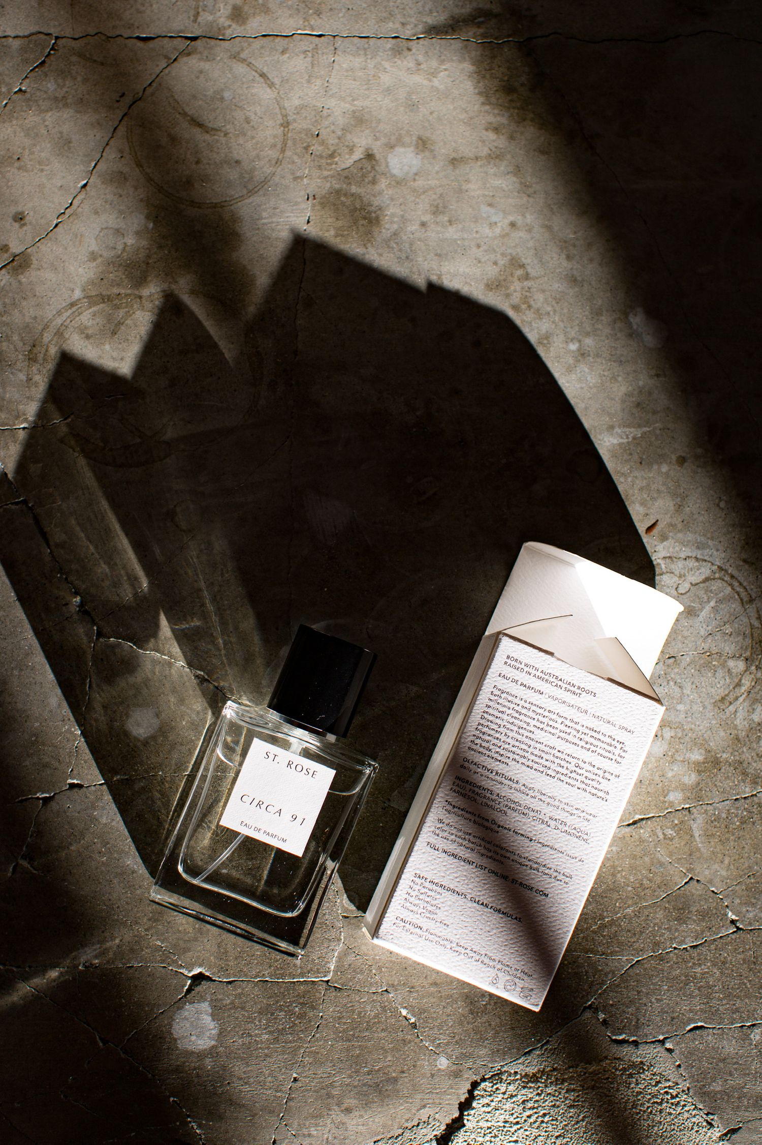 Perfume bottles and product literature arranged on a textured concrete surface in dramatic shadows.