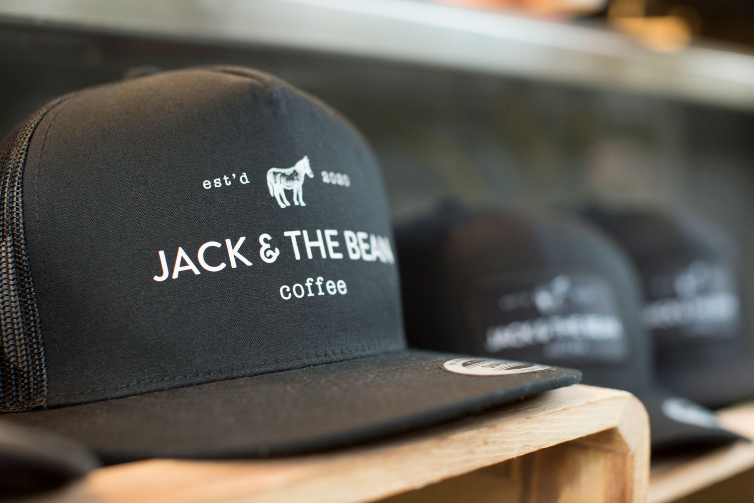 Close-up of black mesh trucker hat with white Jack & The Bean coffee logo.