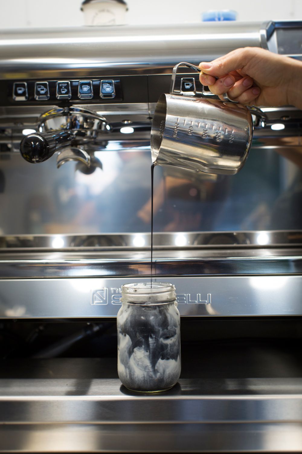 Barista steaming milk with professional espresso machine with jar below.