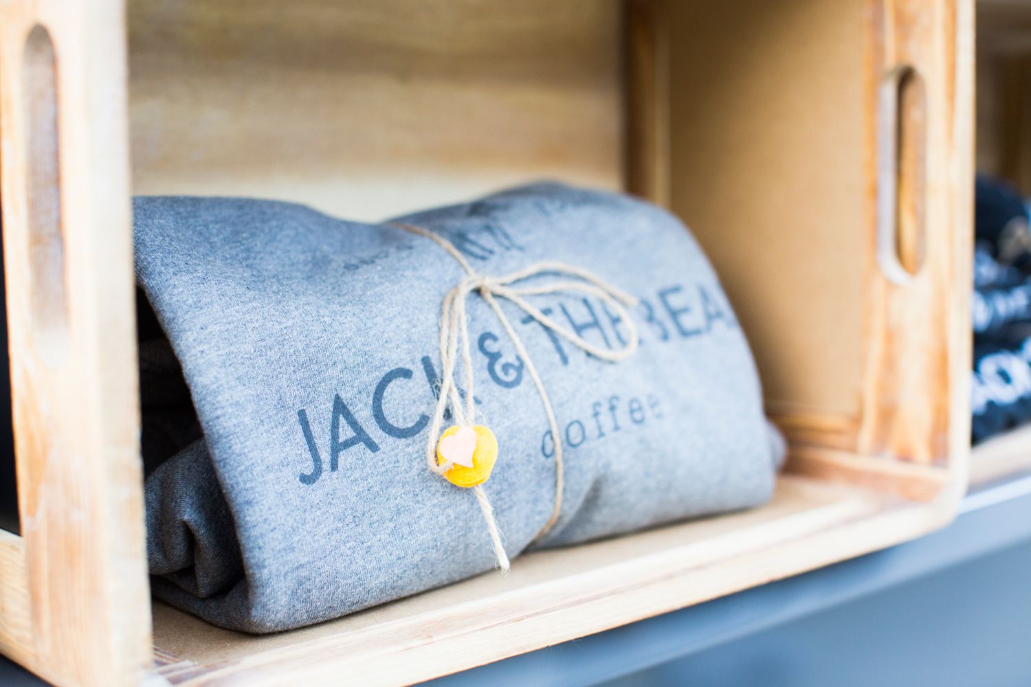 Gray sweatshirt with Jack & The Bean coffee branding folded in wooden display shelf.