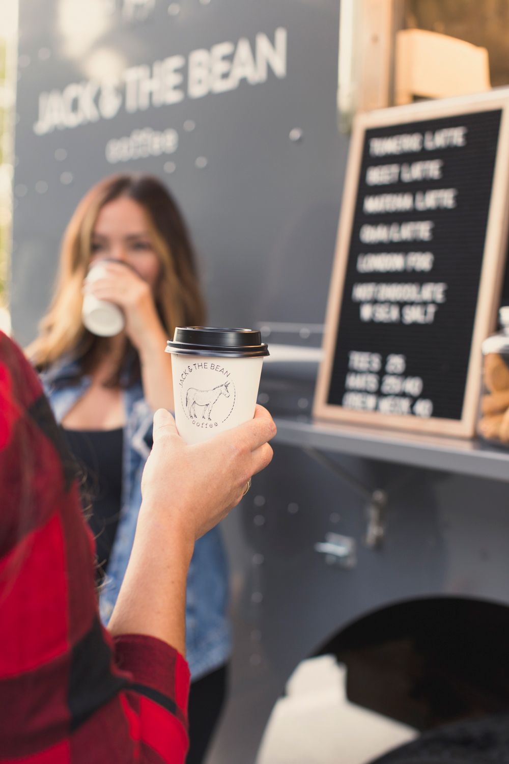 Customer holding branded coffee cup from Jack & The Bean coffee truck with menu board in background.
