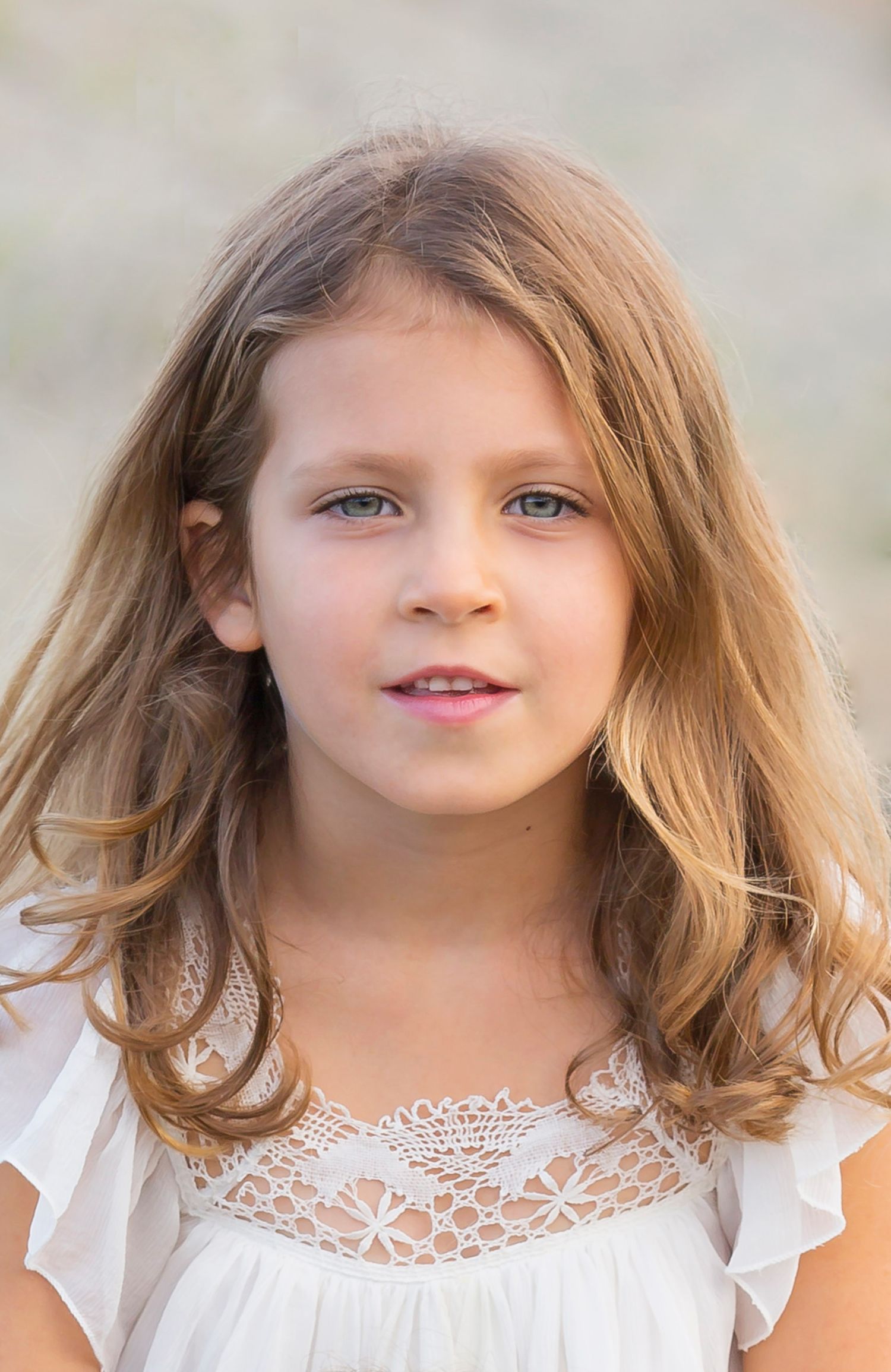 Young girl in white lacy dress with wavy hair photographed outdoors.