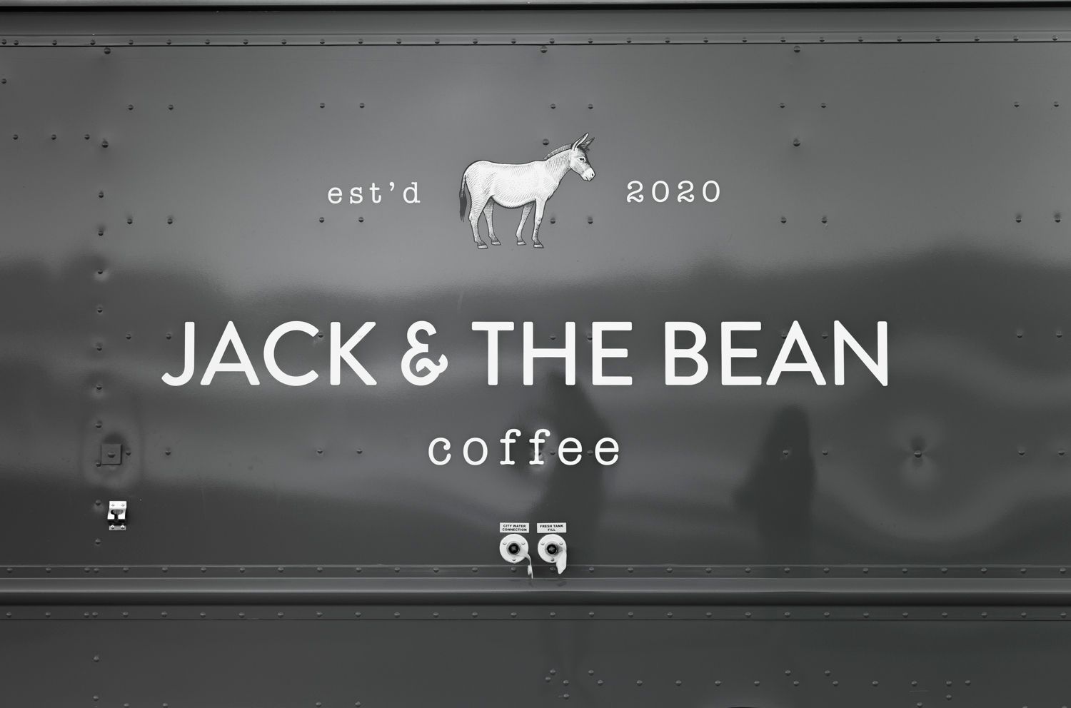 Close up of Jack & The Bean Coffee branding with cow logo on gray truck exterior.