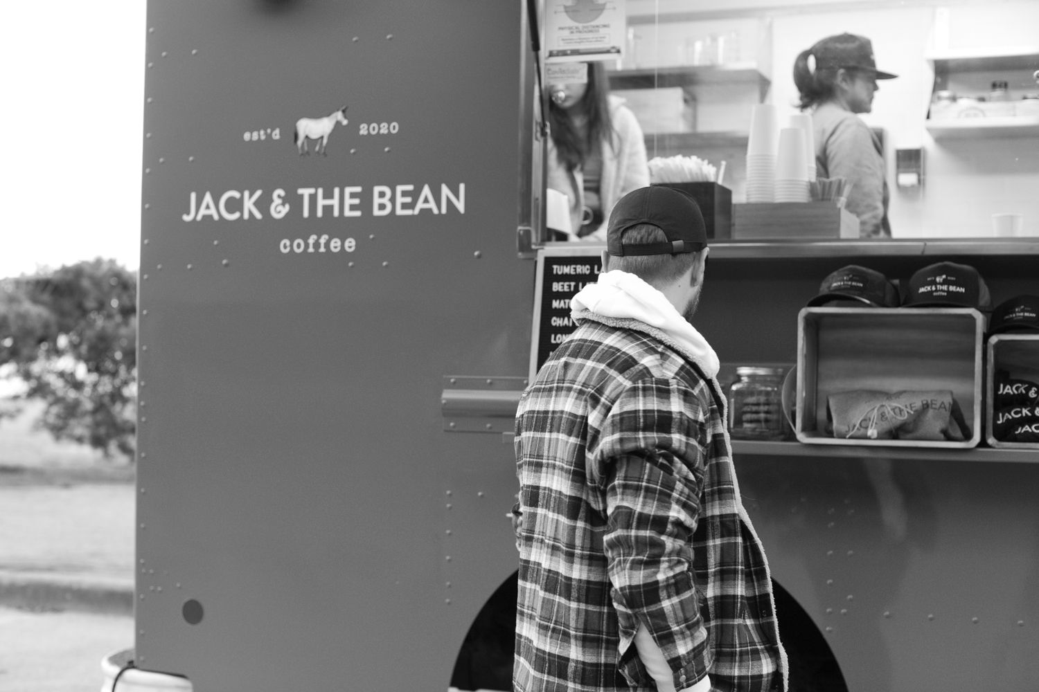 Black and white image of coffee truck with customer at service window.