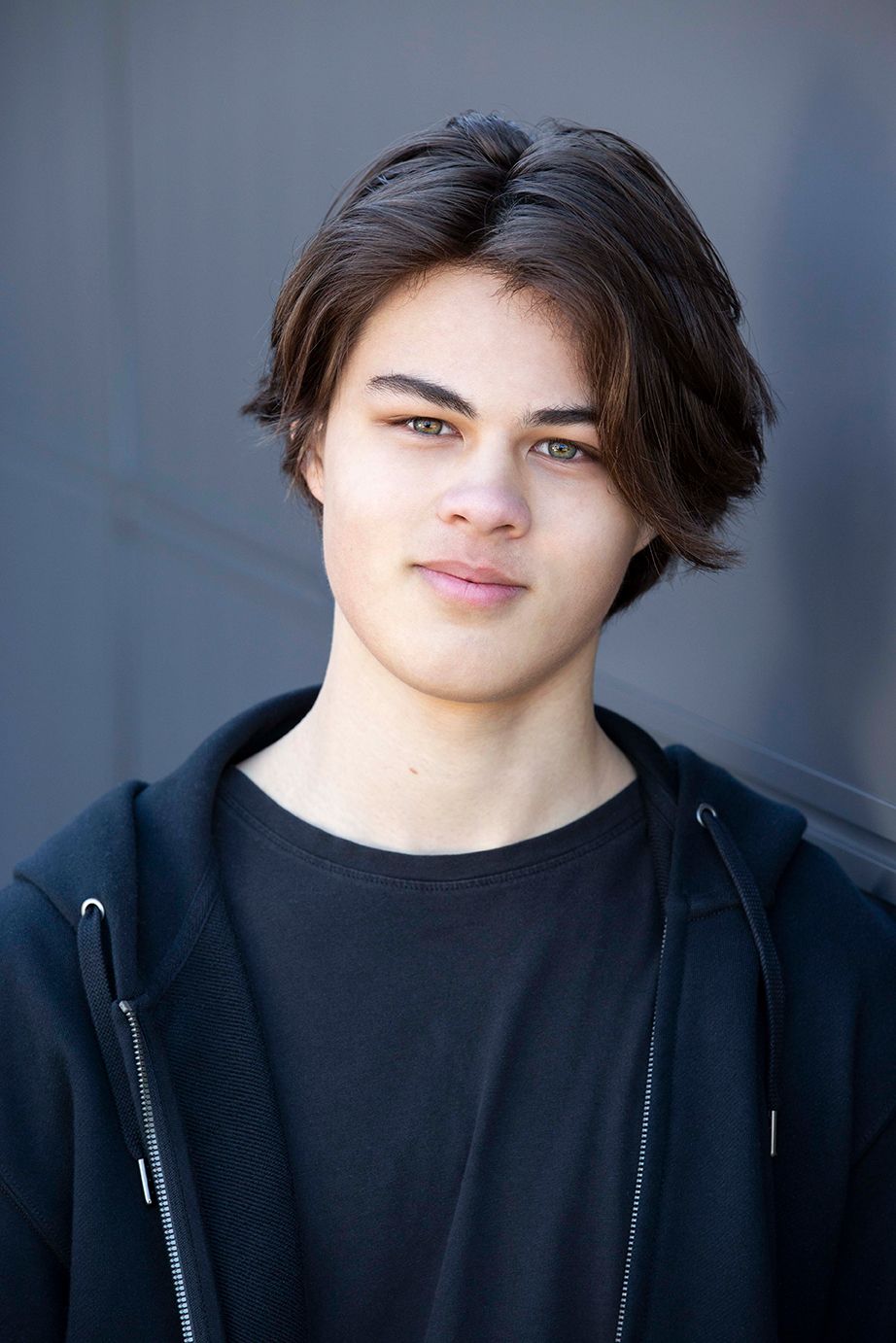 Close-up shots showing casual style with black hoodie against studio backdrop.