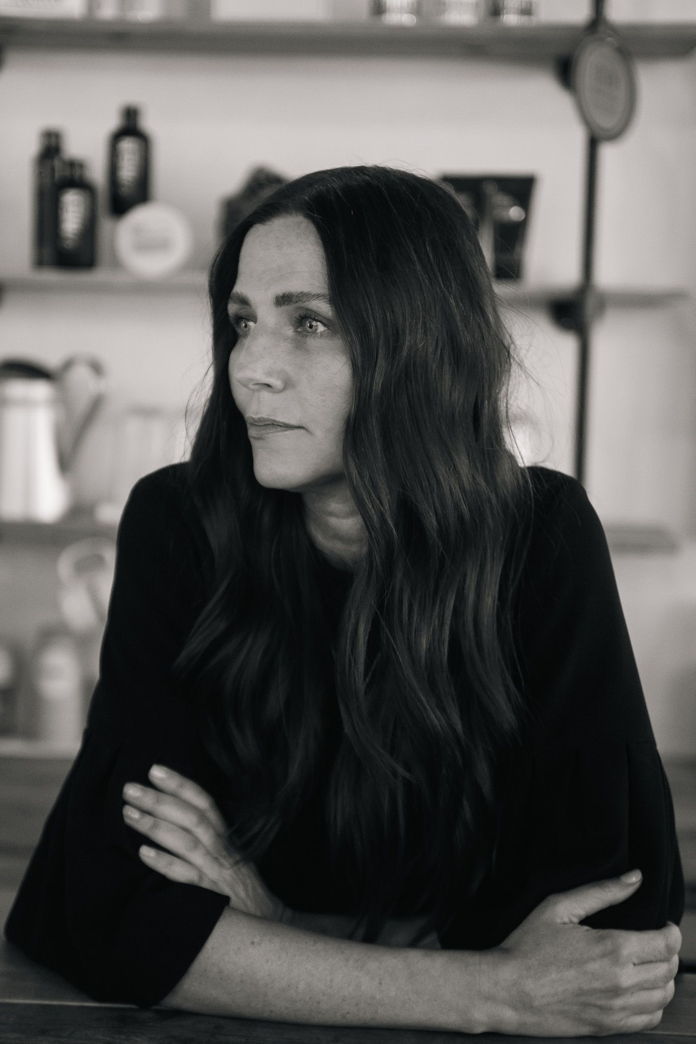 Black and white portrait of woman with long dark hair sitting at counter in kitchen setting.