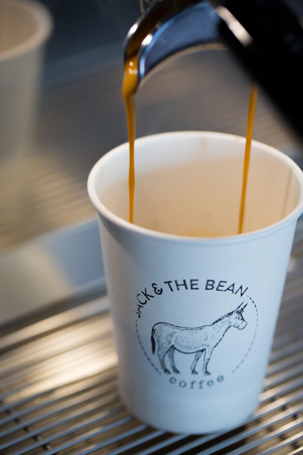 Coffee being poured into a white cup with Jack & The Bean logo featuring a donkey illustration.