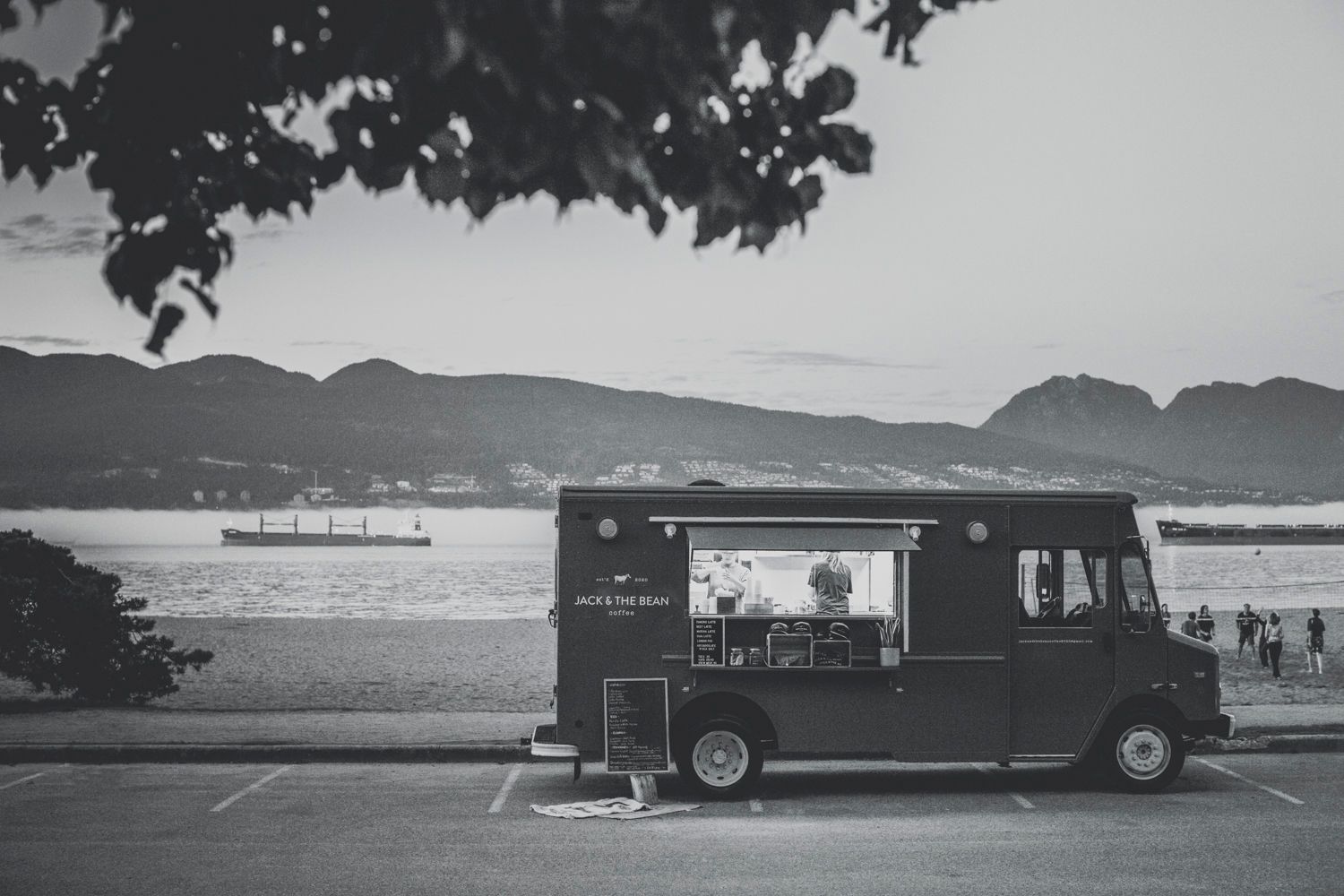 Black and white landscape view of parked vehicles and mountains near coastal area.