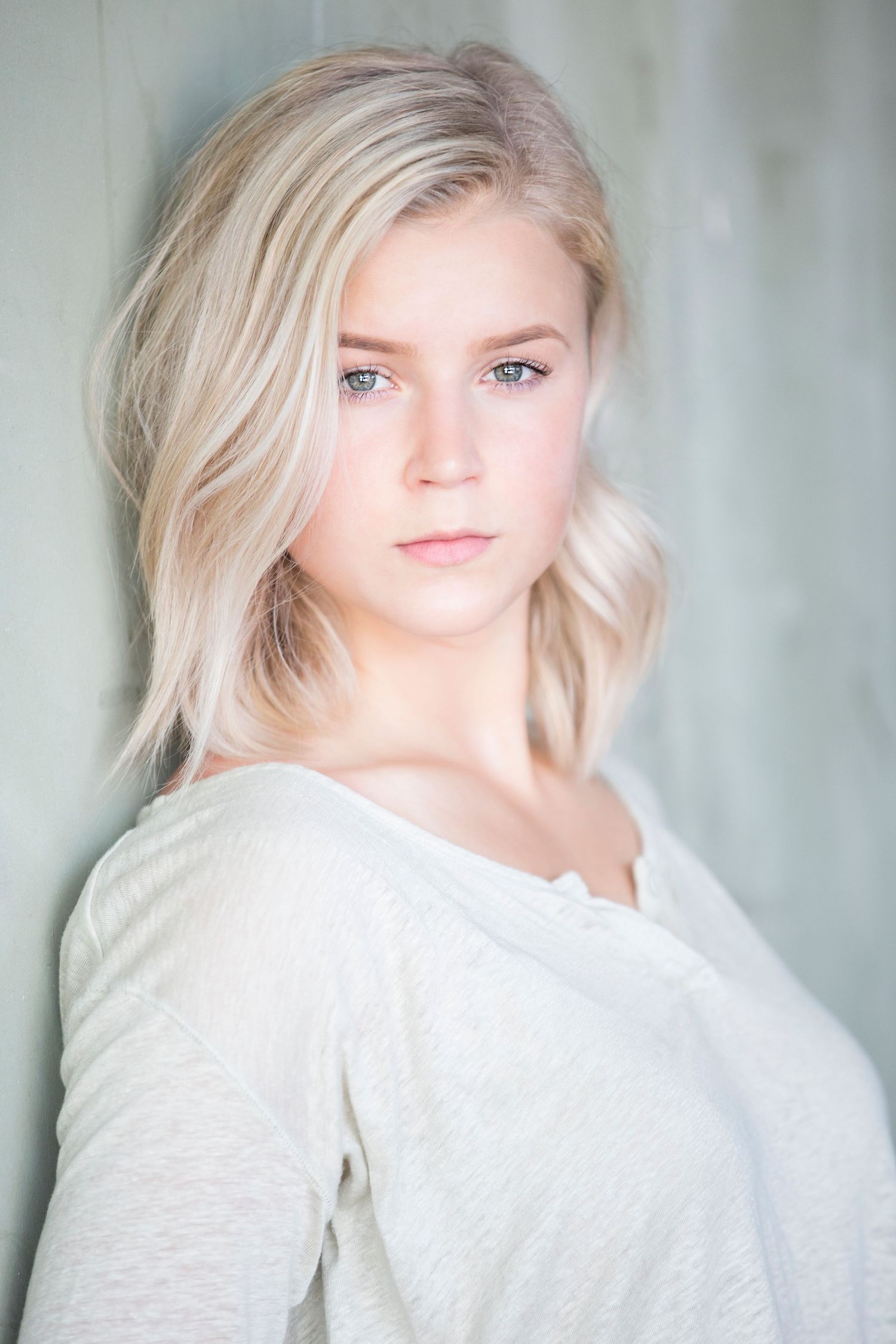 Soft portrait in white top against light background.
