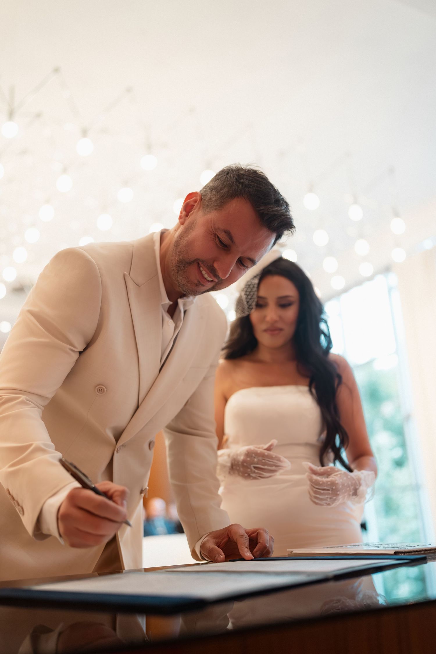A couple signs their marriage license at a wedding ceremony while wearing formal attire.