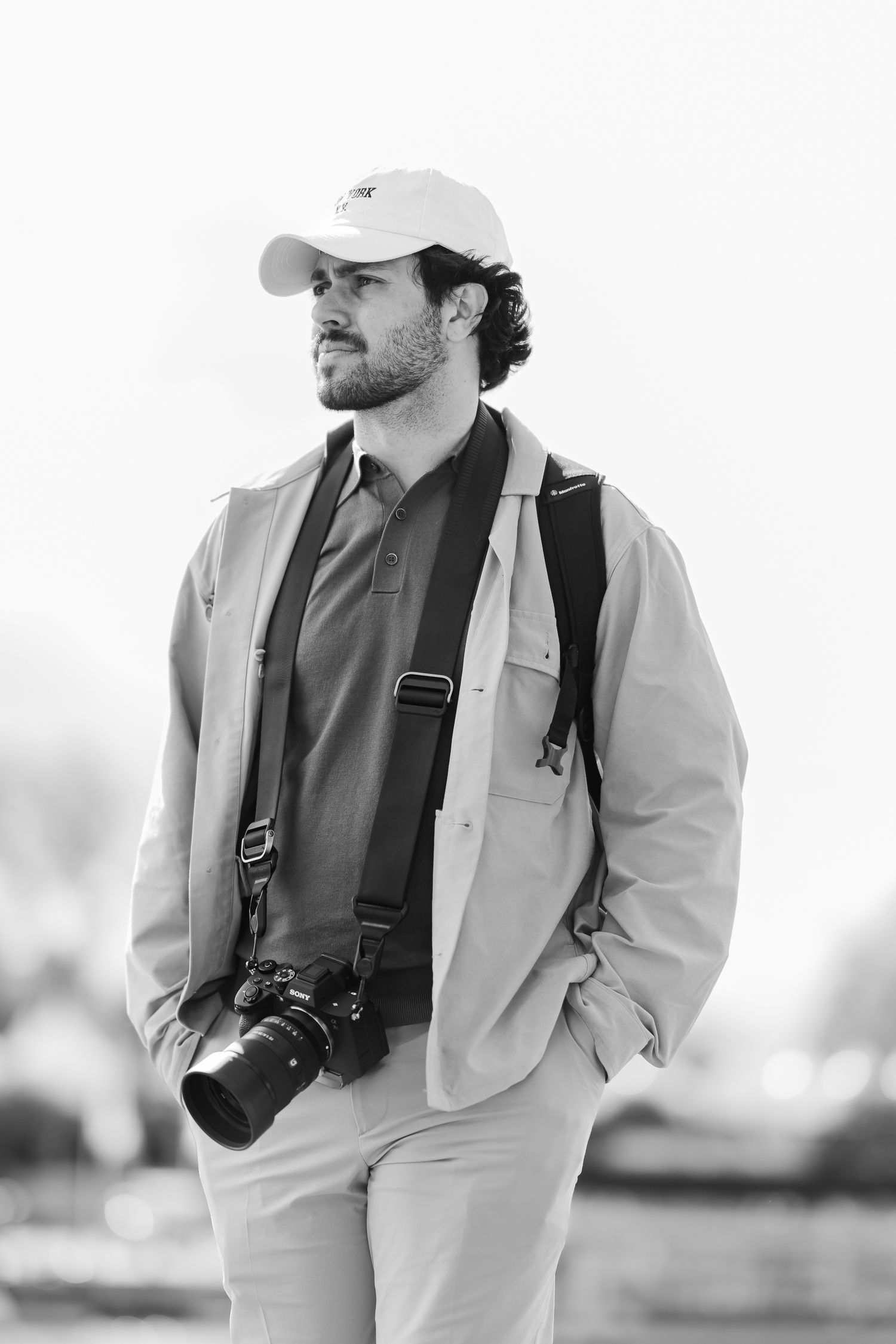 Photographer in casual wear with camera around neck posing in black and white portrait.