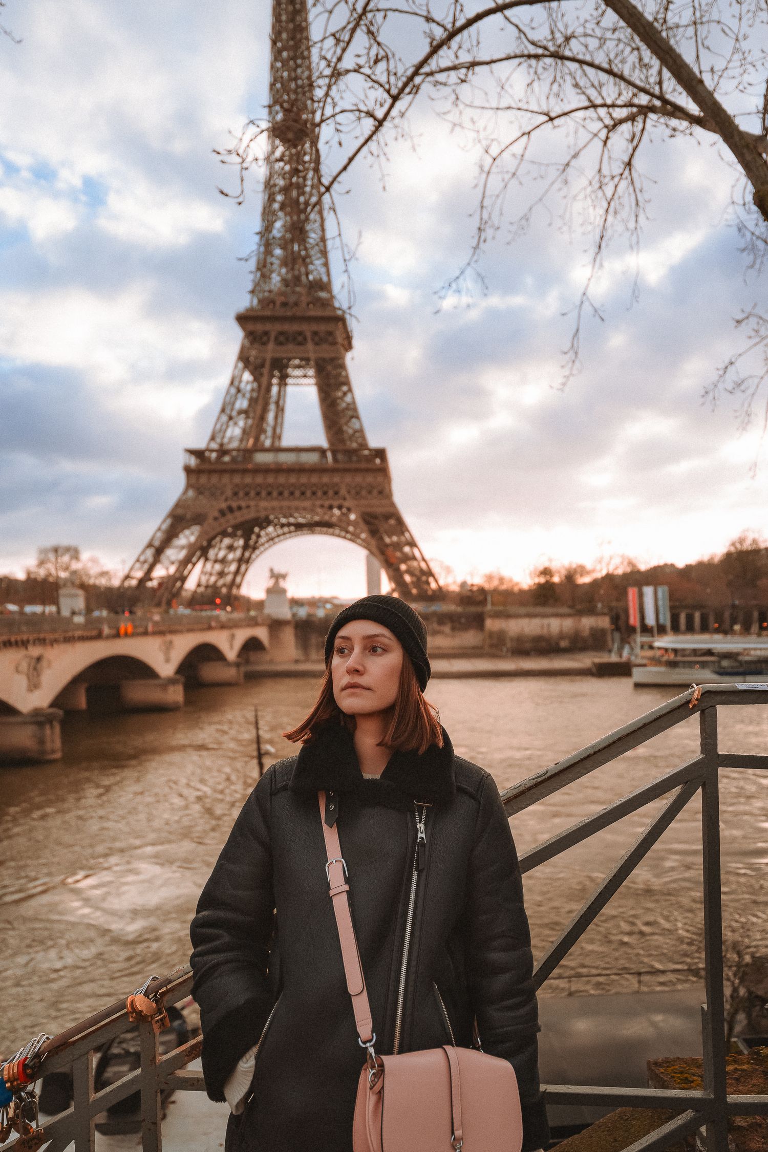 Tourist in black coat gazing at Eiffel Tower from riverside during cloudy autumn day.