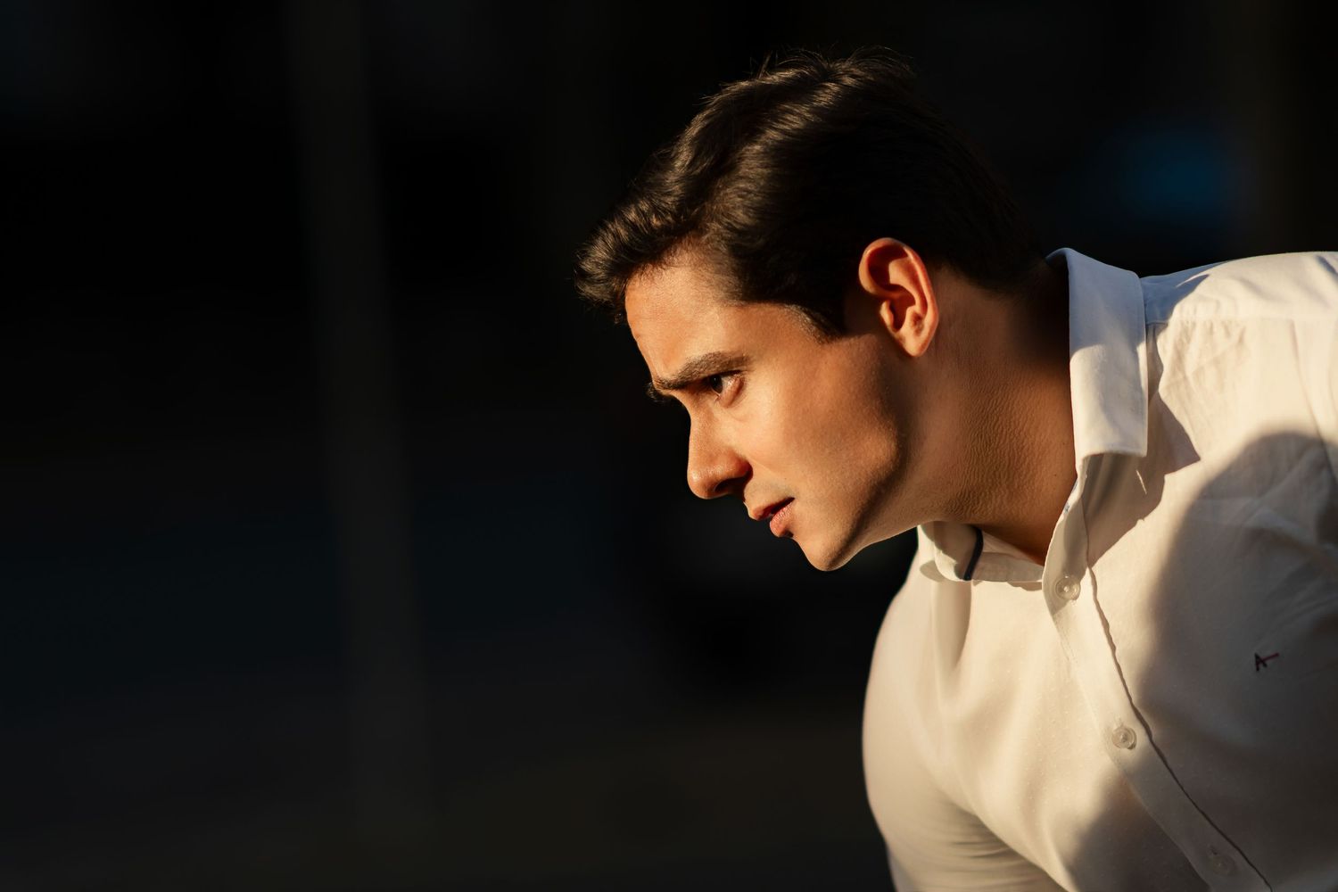 A person in a white shirt works at a computer station in a dimly lit room.