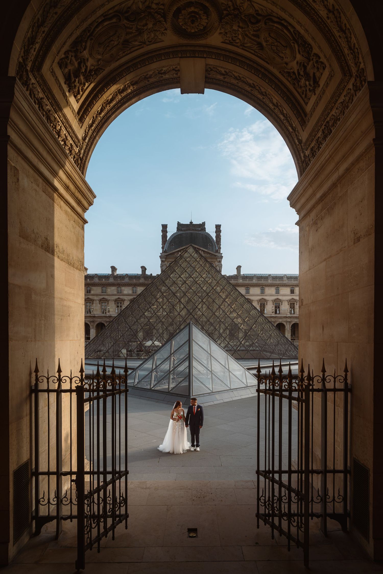 A series of silhouetted archways frame views of the iconic Louvre Pyramid in Paris at dusk.