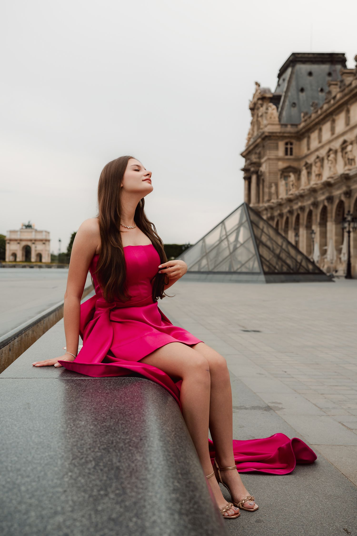 Fashion portrait in a vibrant pink dress at the Louvre pyramid in Paris.
