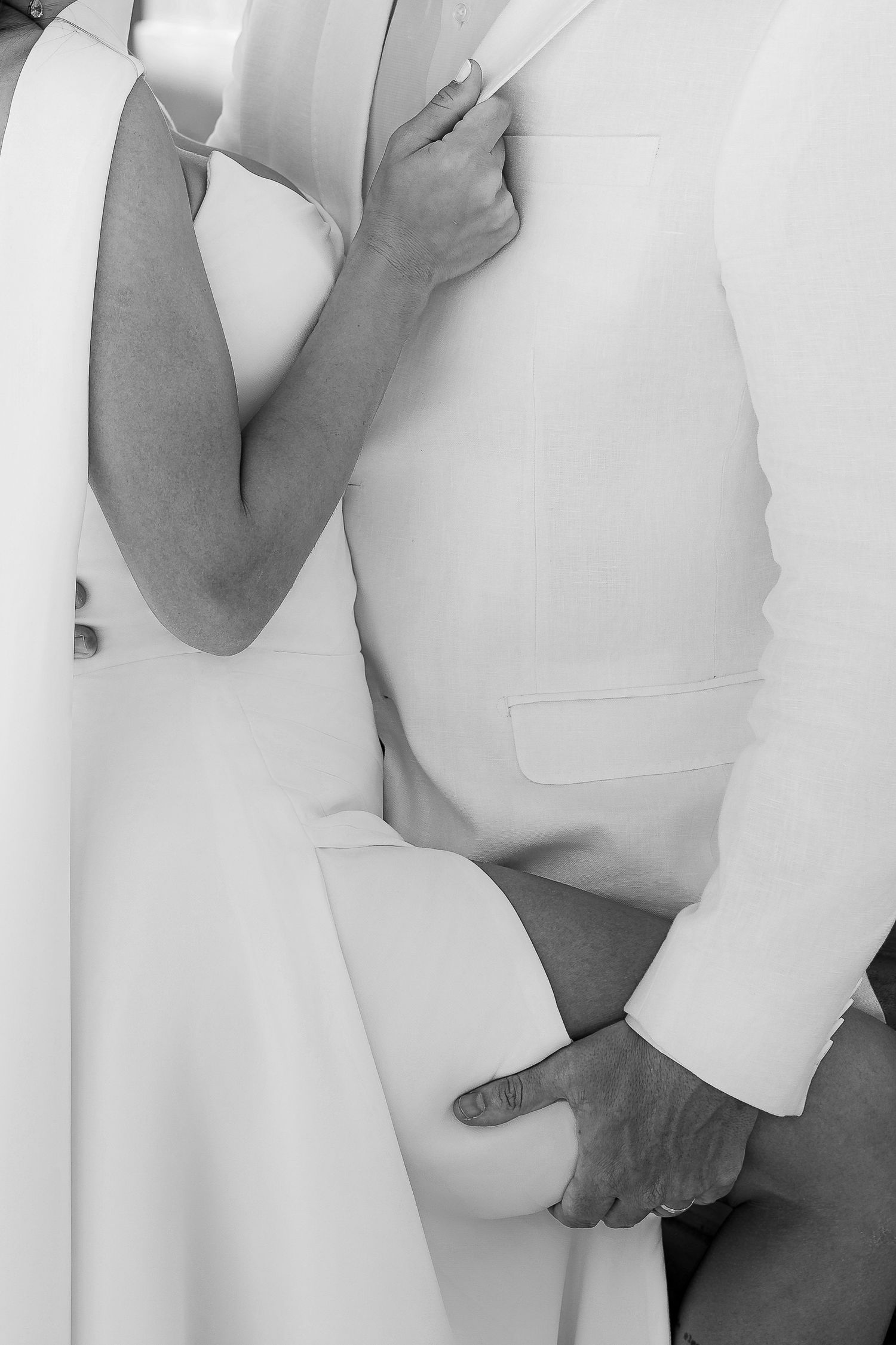 Black and white close-up of a couple in wedding attire embracing, showing only their torsos in elegant formal wear.