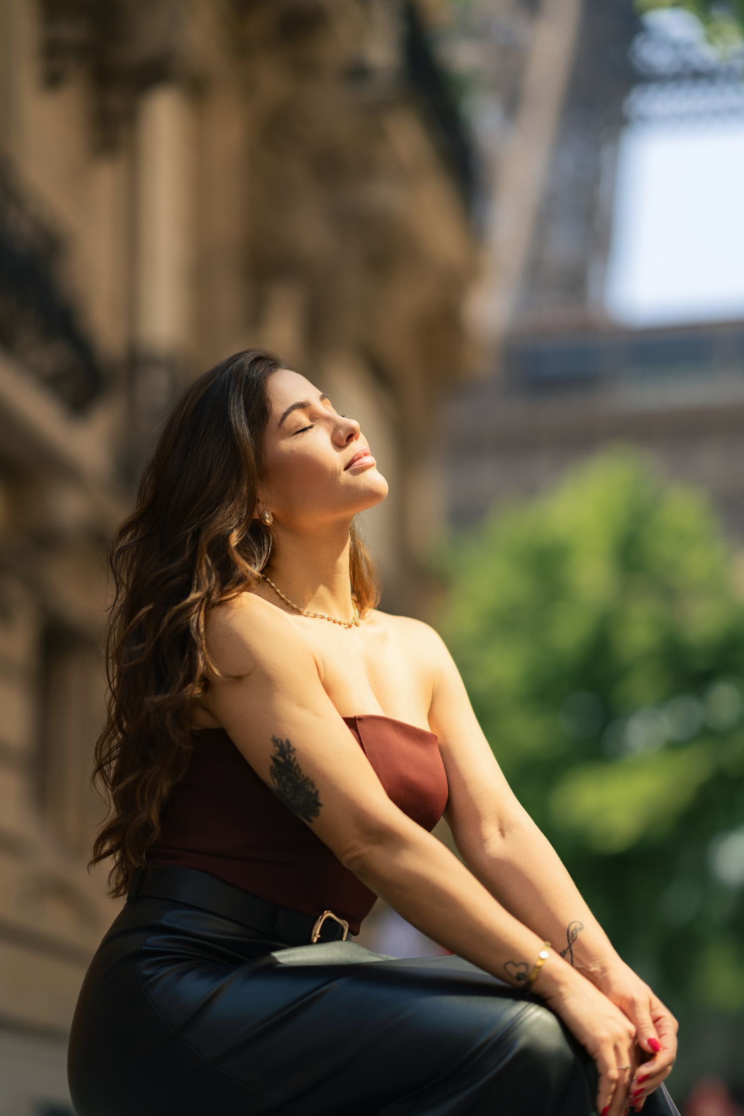 Portrait of someone in a brown top basking in sunlight against historic architecture.