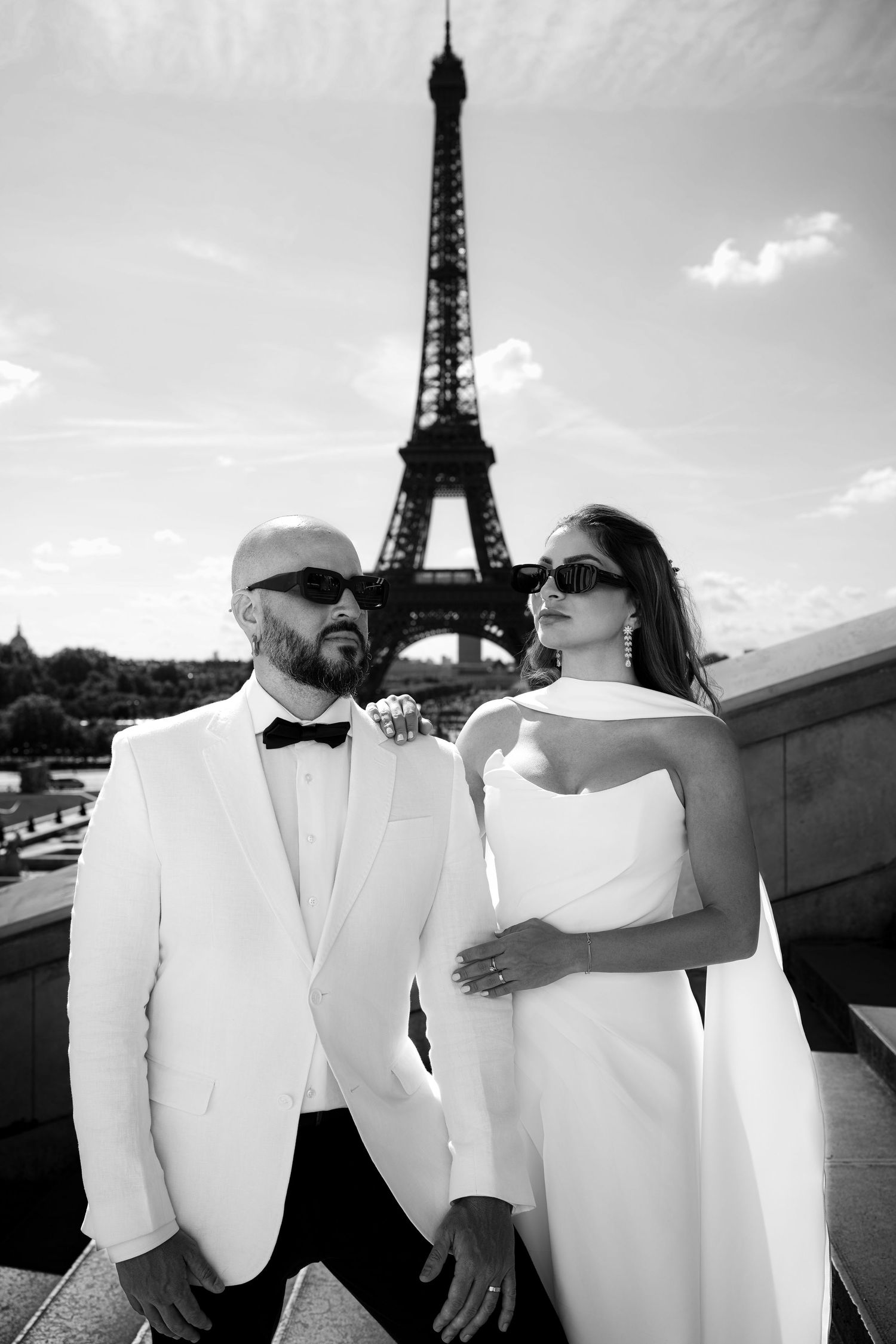 Romantic black and white photo series of a couple in white outfits posing near the Eiffel Tower in Paris.
