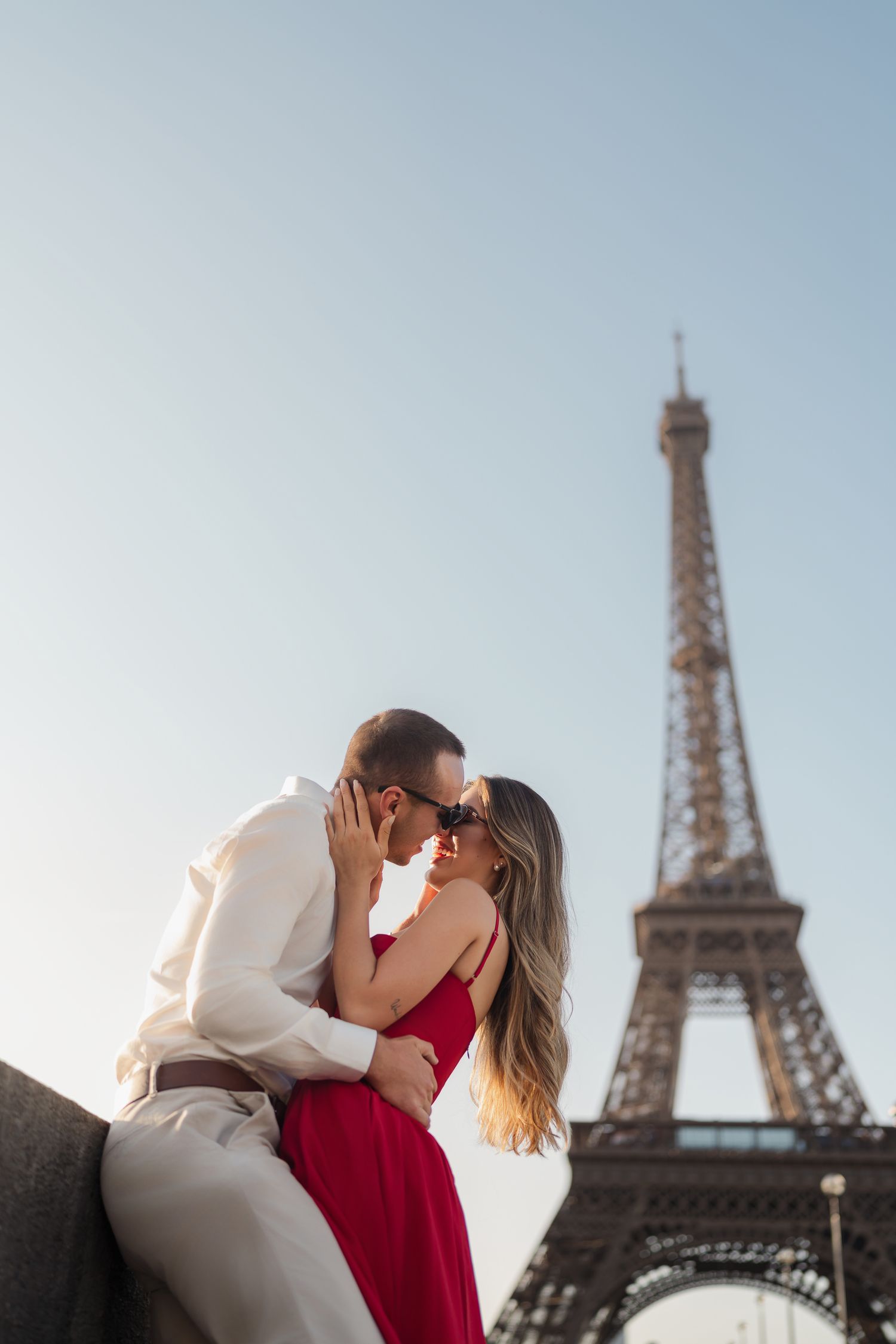 Romantic couple embraces near the Eiffel Tower in Paris on a bright sunny day with iconic landmark in background.