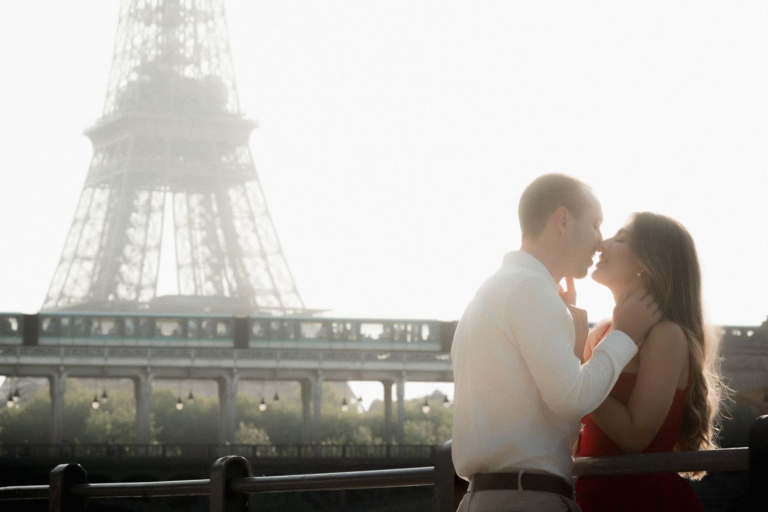 A romantic couple shares an intimate moment in front of the Eiffel Tower during a misty Parisian sunset.