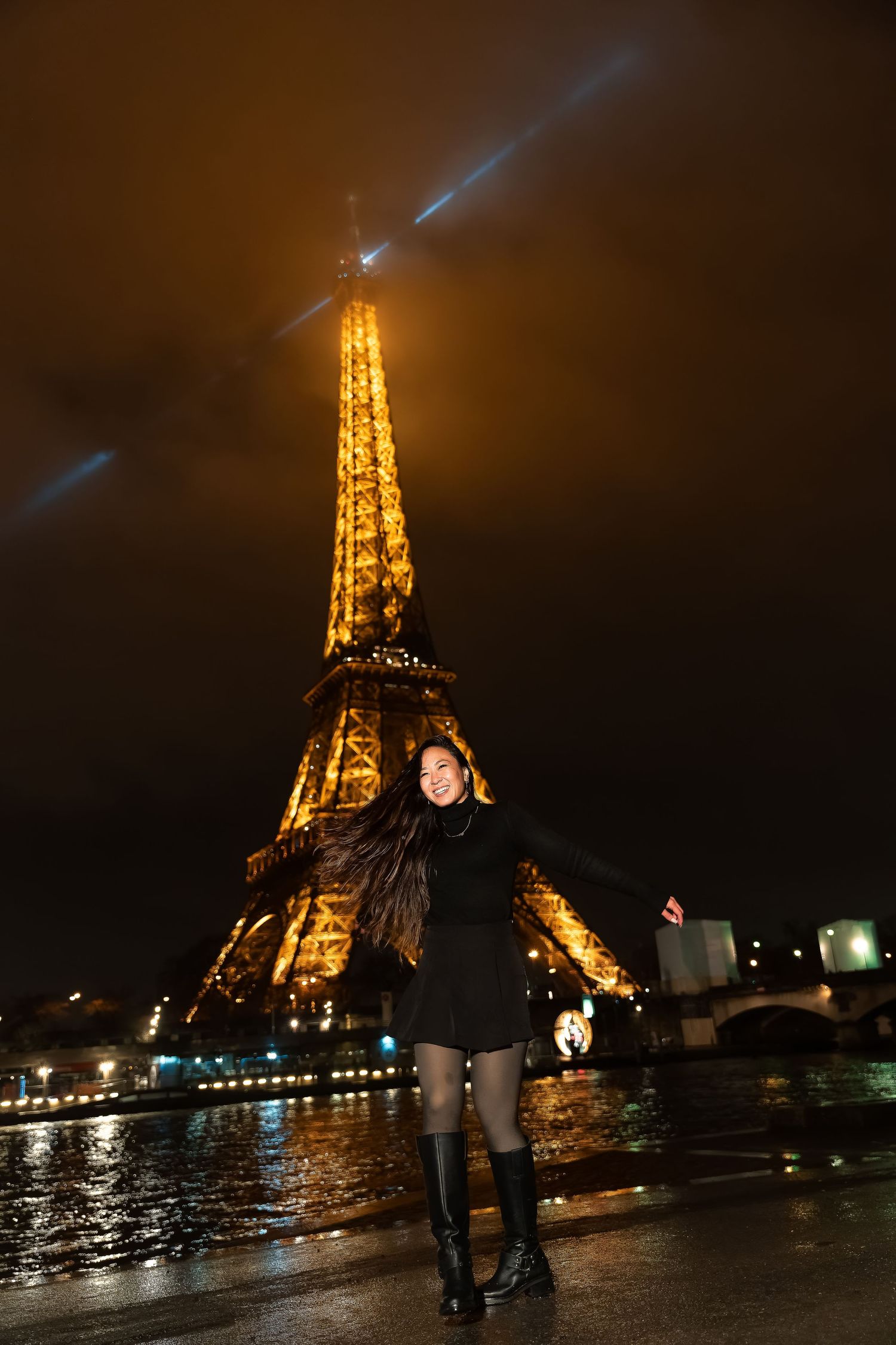 Illuminated Eiffel Tower glows golden against dark night sky with wet reflective pavement in Paris.