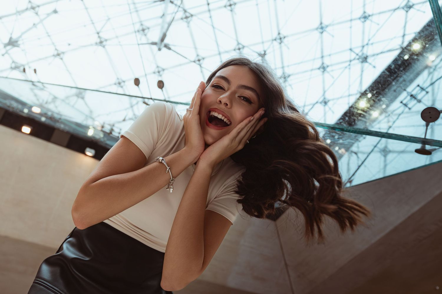 Collage of five photos showing someone posing playfully against a glass ceiling with geometric patterns.