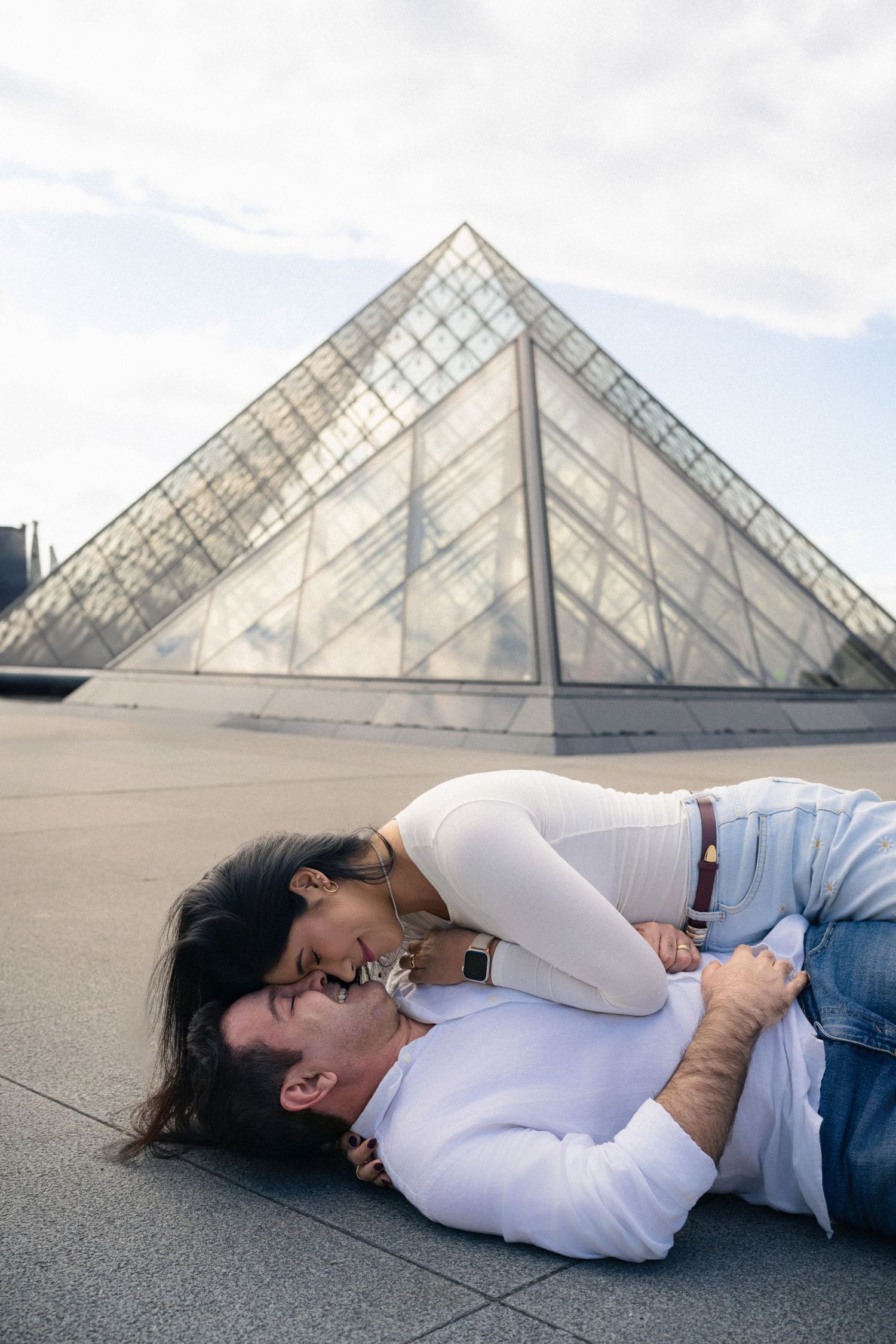 A series of five photos showing someone lying on the ground in front of the Louvre pyramid in Paris.