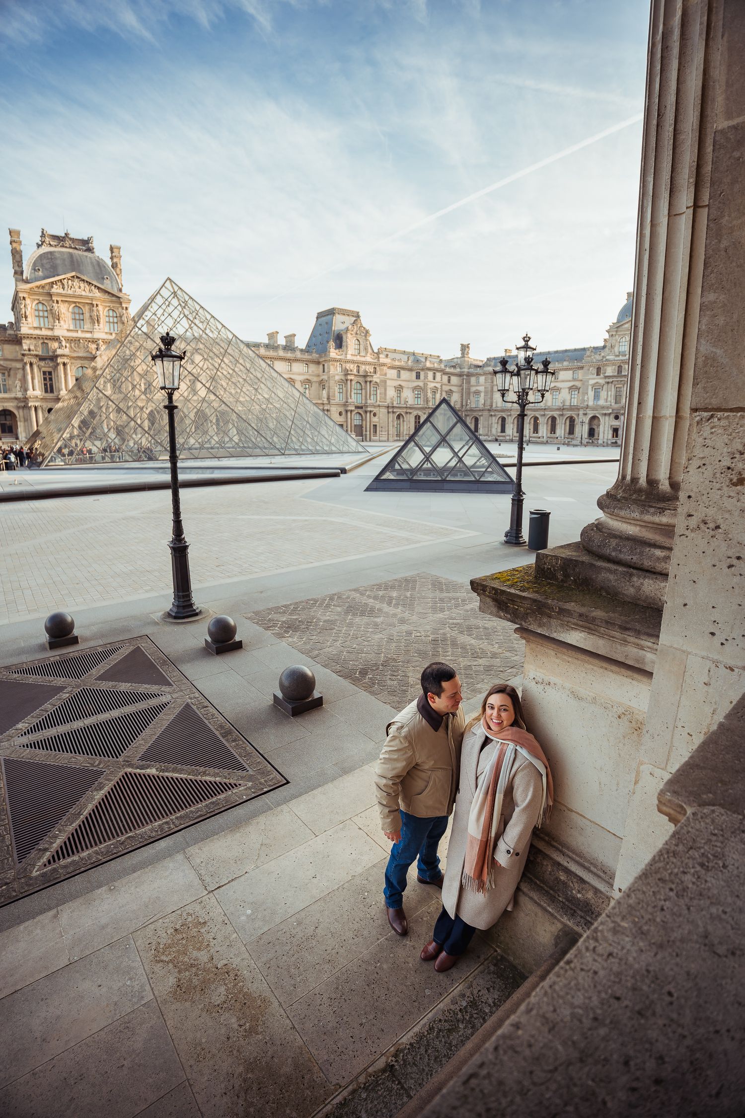 Couple stands on stairs near Louvre pyramid in Paris during sightseeing.