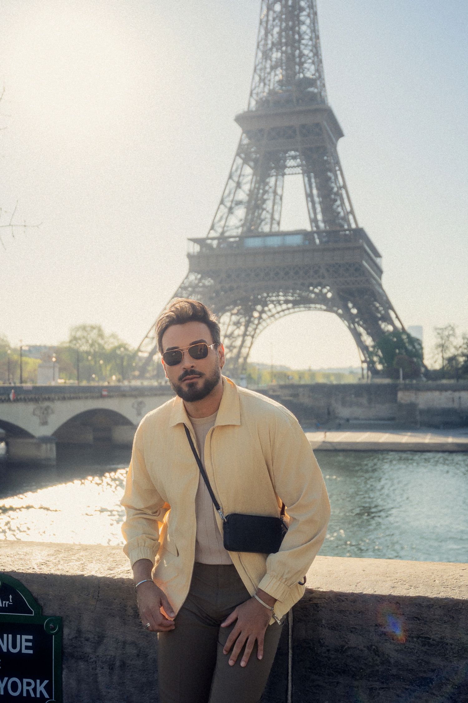 Person in casual attire poses by Seine River with Eiffel Tower in background.