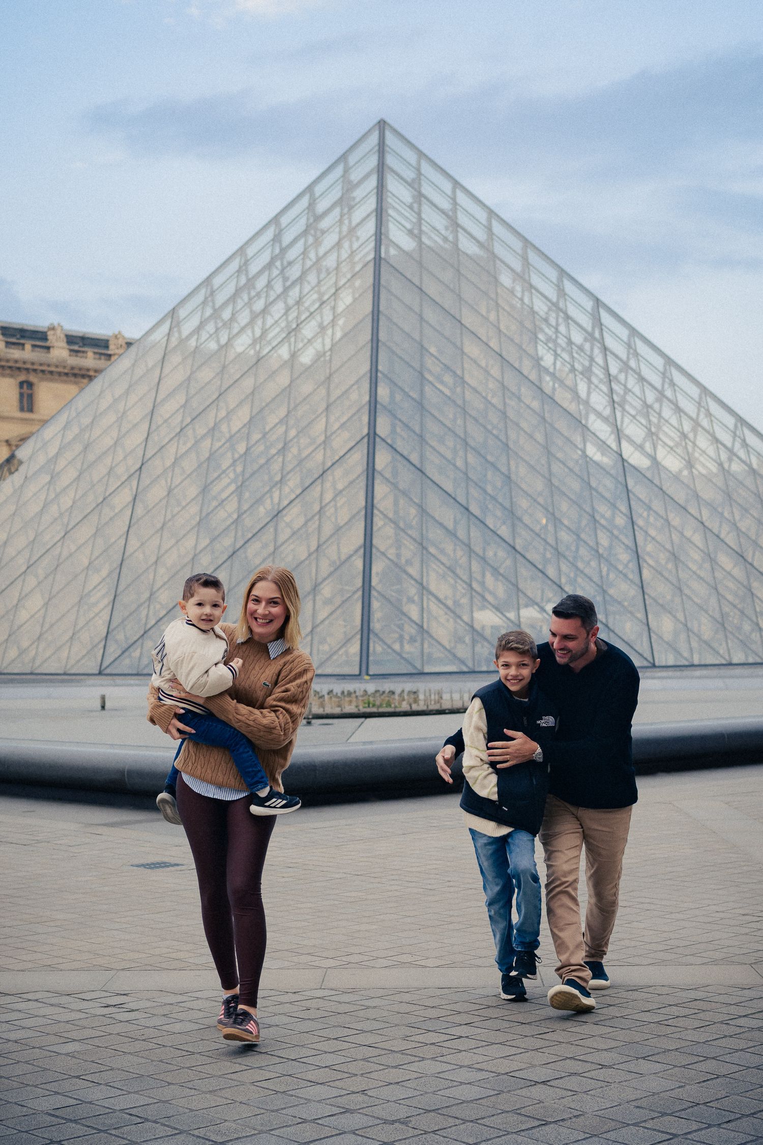 Family walking together outside famous Louvre pyramid in Paris.