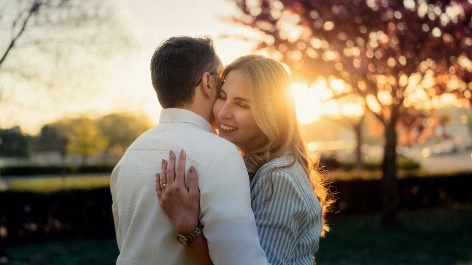 Intimate couple embrace during golden sunset in park setting.