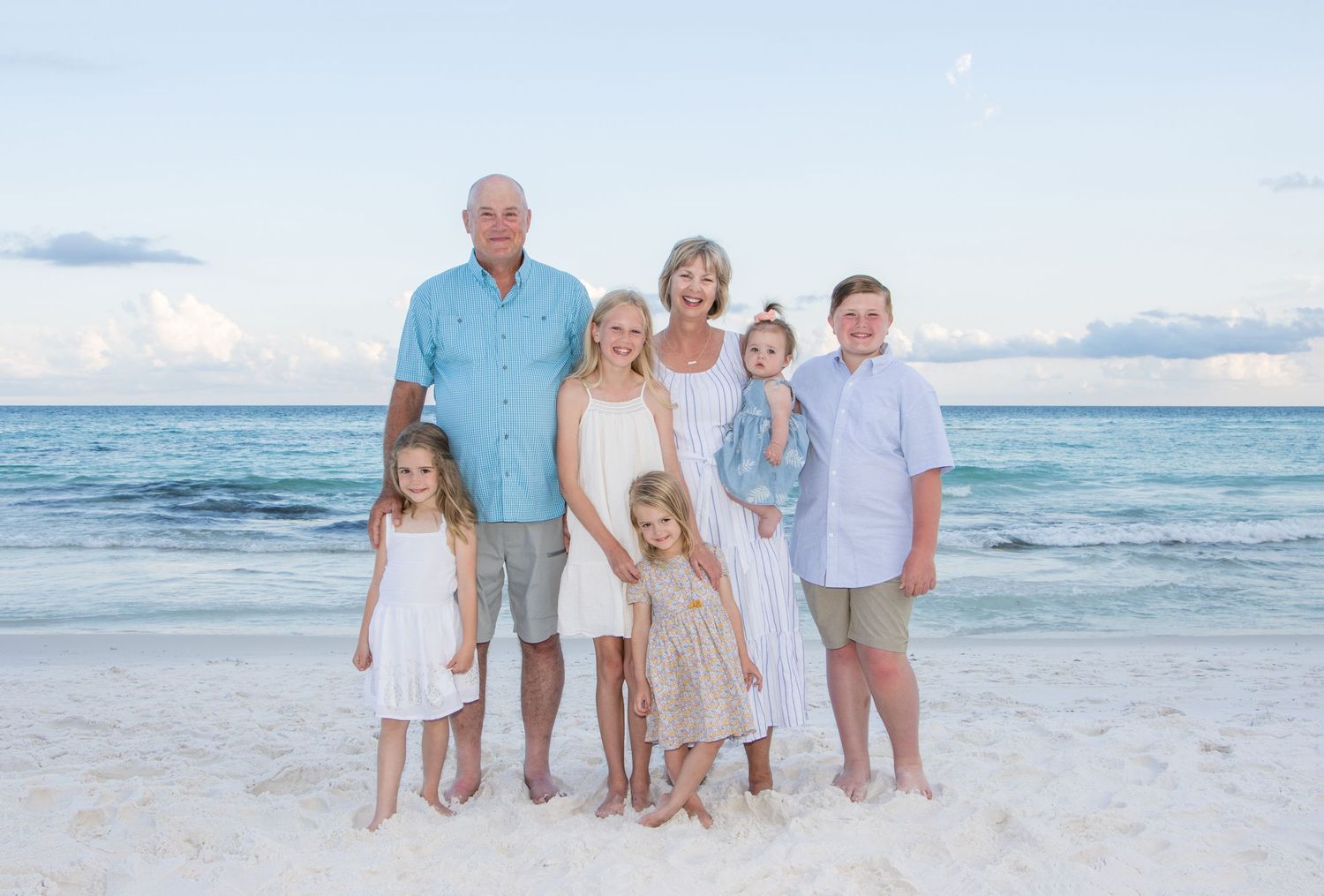 Extended family group wearing coordinated blue and white outfits posing on a sunny beach.