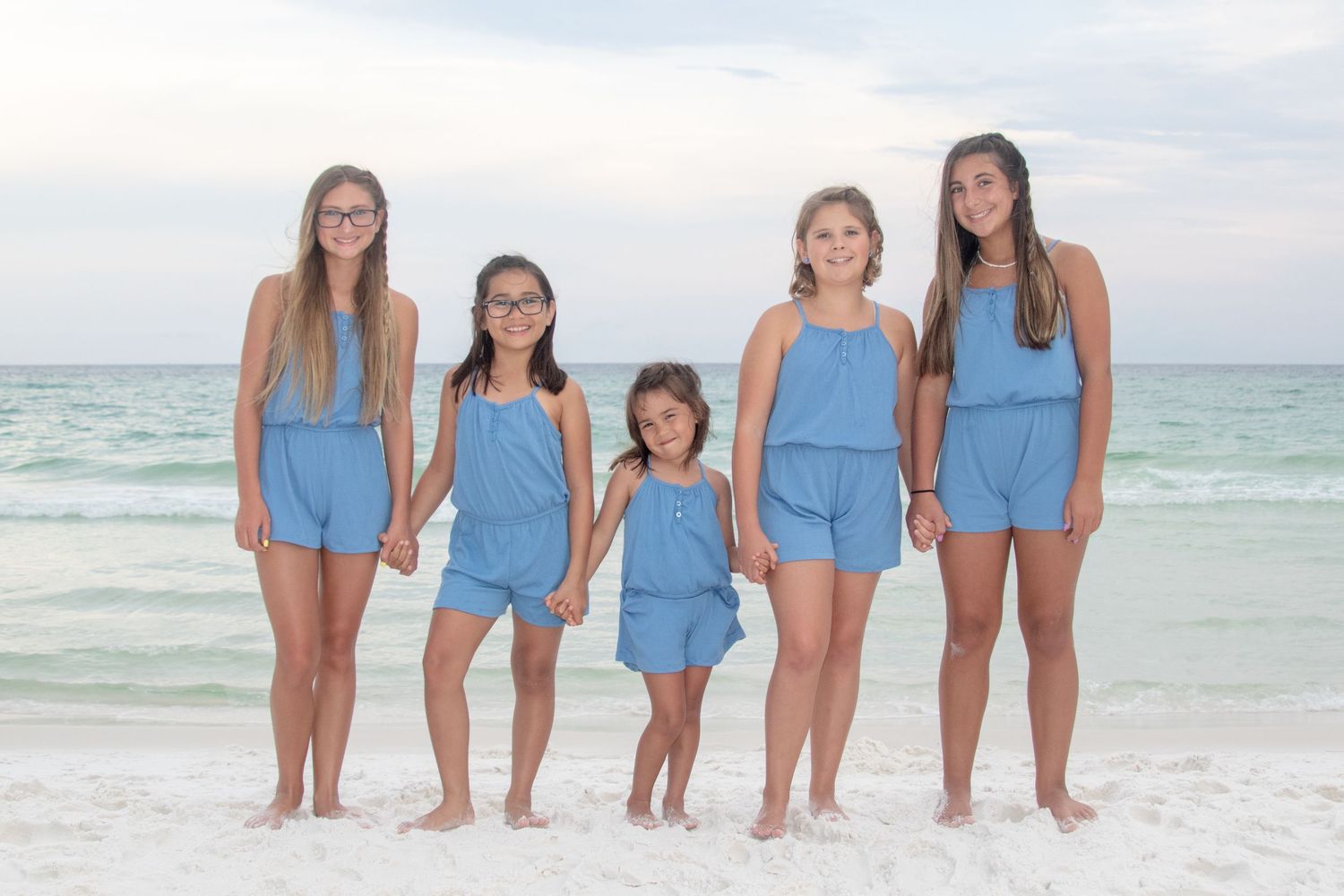A group of people in coordinating blue outfits standing together on a sunny beach by the ocean.