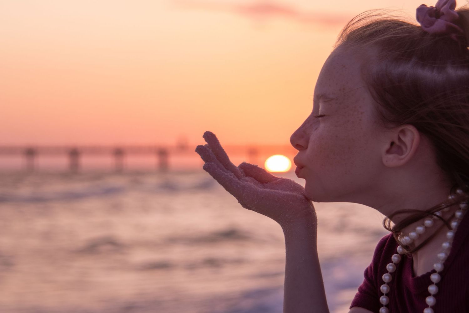 Silhouette of a young girl against orange sunset sky at beach.