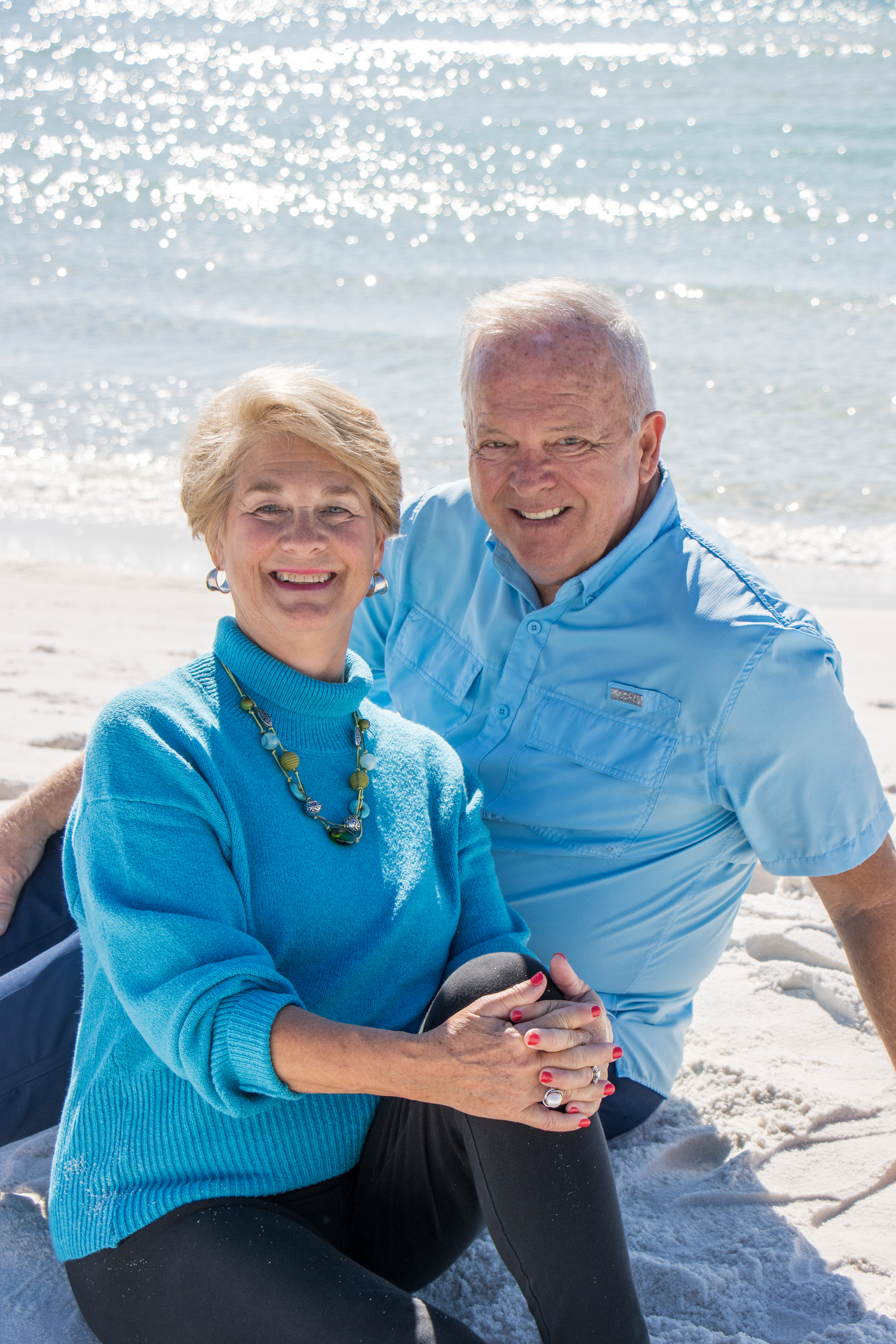 Couple in matching blue outfits share a tender moment on sunny beach.