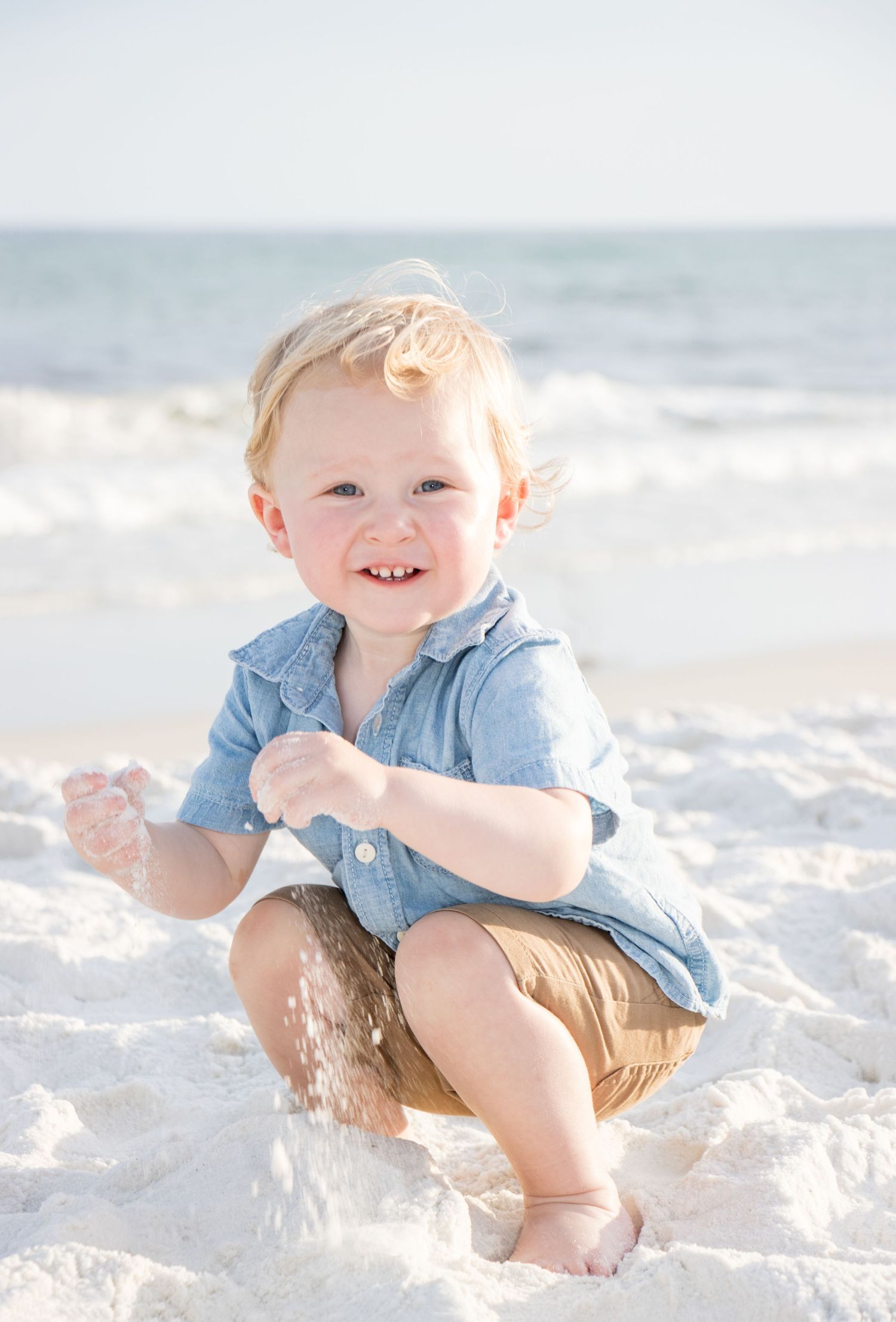 Young child in blue shirt plays in white sand at the beach.