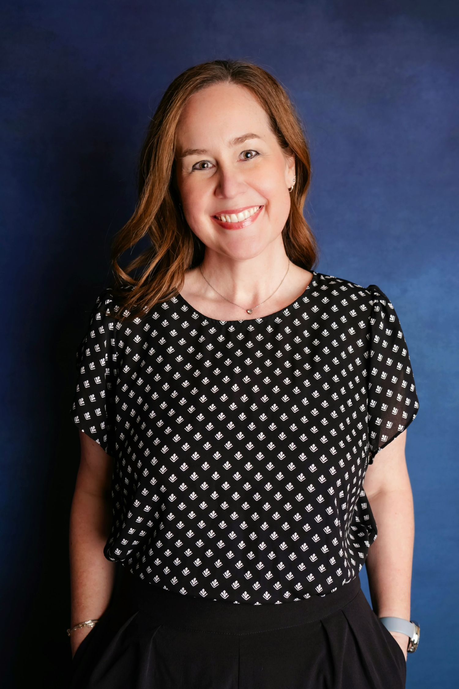 Professional studio portrait of Jolie wearing a polka dot blouse and dark skirt against a blue backdrop.