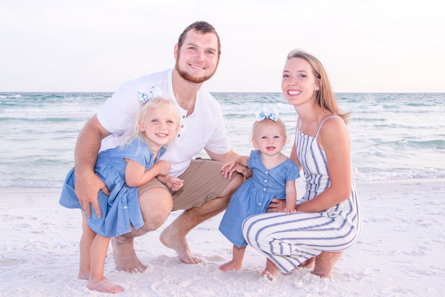 Family posing together on beach with ocean waves in background.