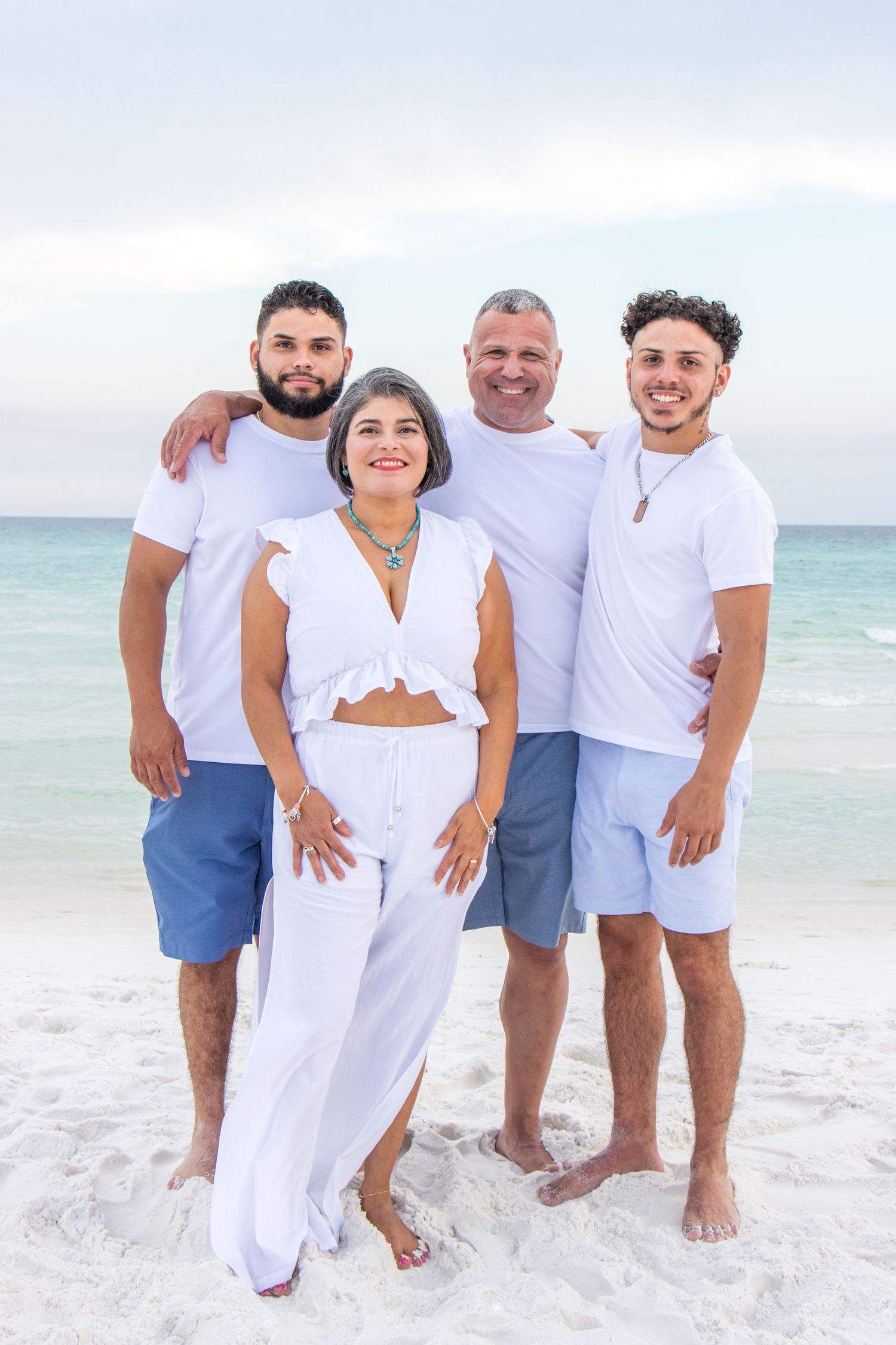 Group wearing white and blue casual outfits poses together on sunny beach.