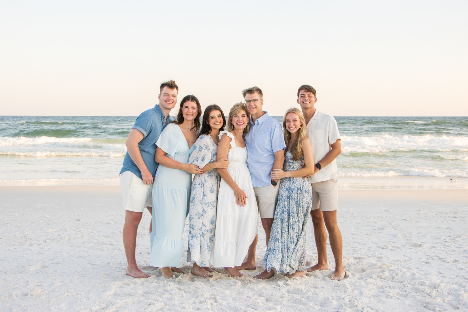 Large family group in coordinated light blue and white clothing gathered on a sunny beach.
