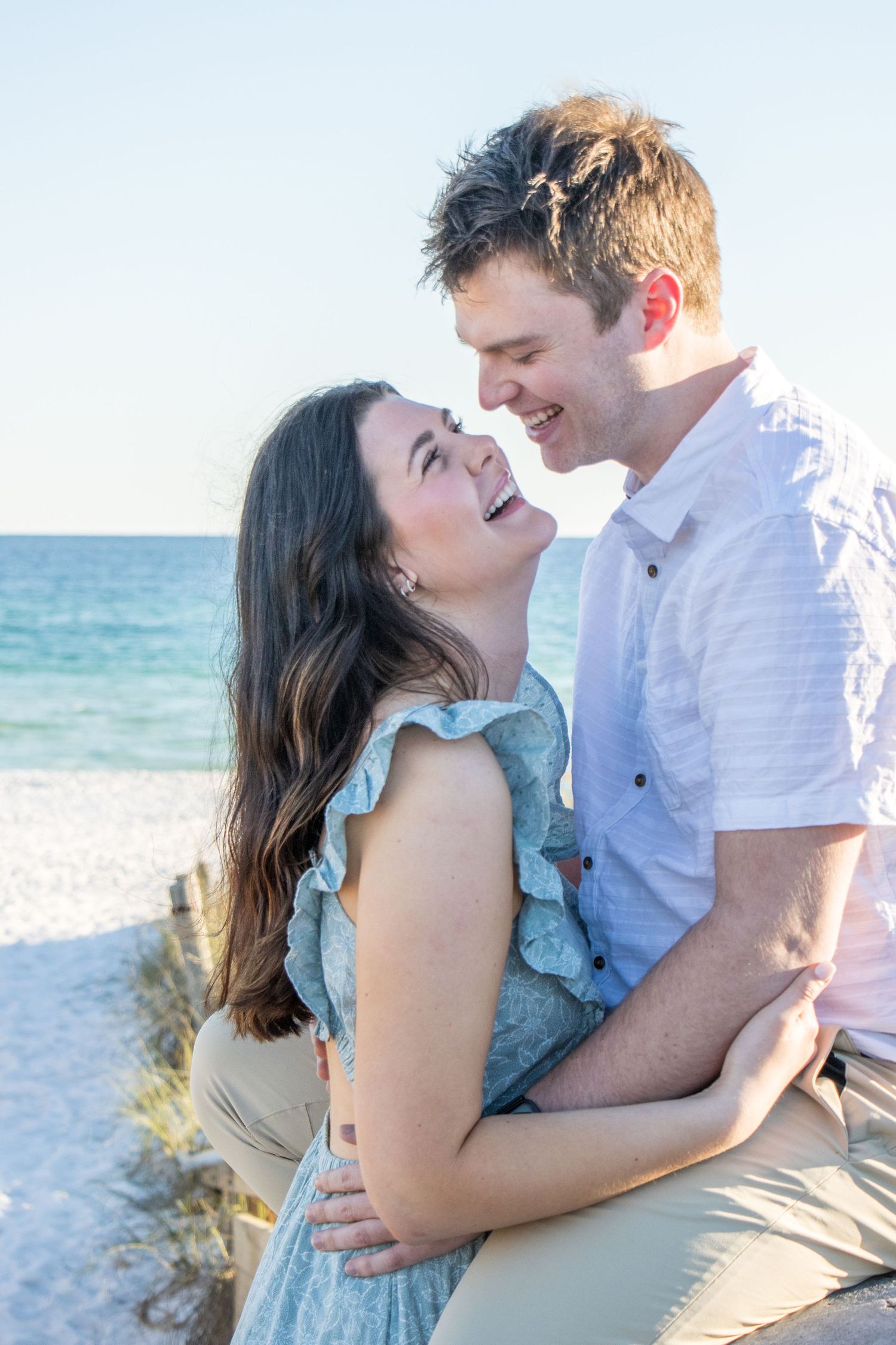 Romantic couple embracing and laughing together during sunset photoshoot on a sandy beach.