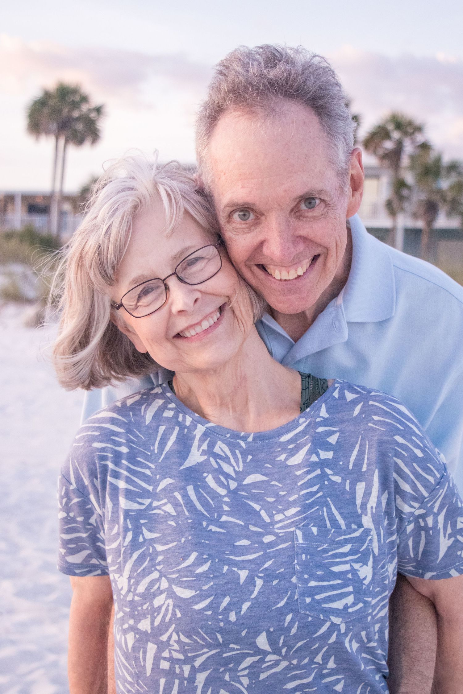 Couple in blue and white outfits share intimate moment on beach at sunset.